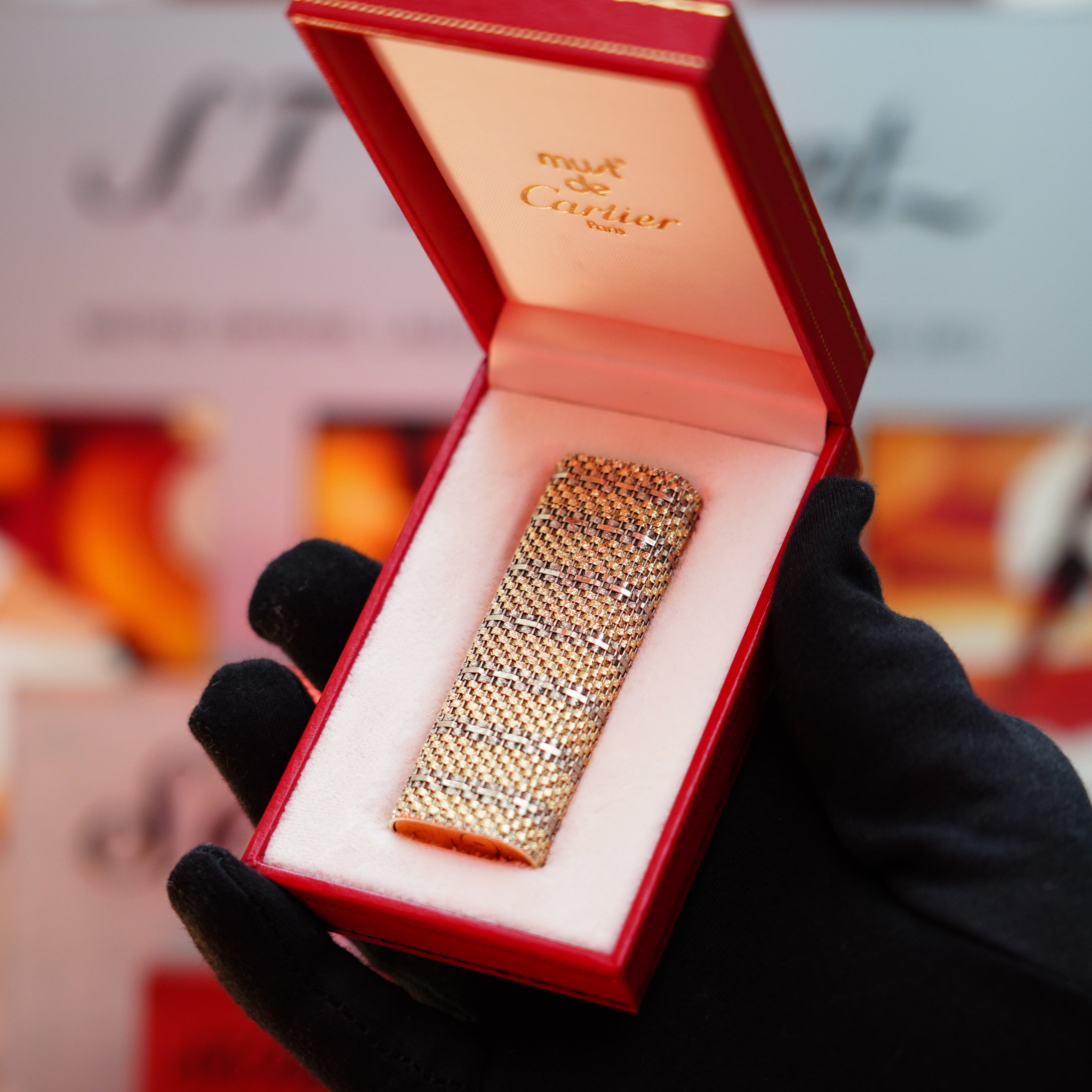 A gloved hand holds an open red box, unveiling a rare collectible: a Vintage 1982 Cartier Solid 18k Gold Jacket Basket Lighter, featuring "myst de Cartier" elegantly inscribed on the inside lid and adorned with sparkling diamonds.