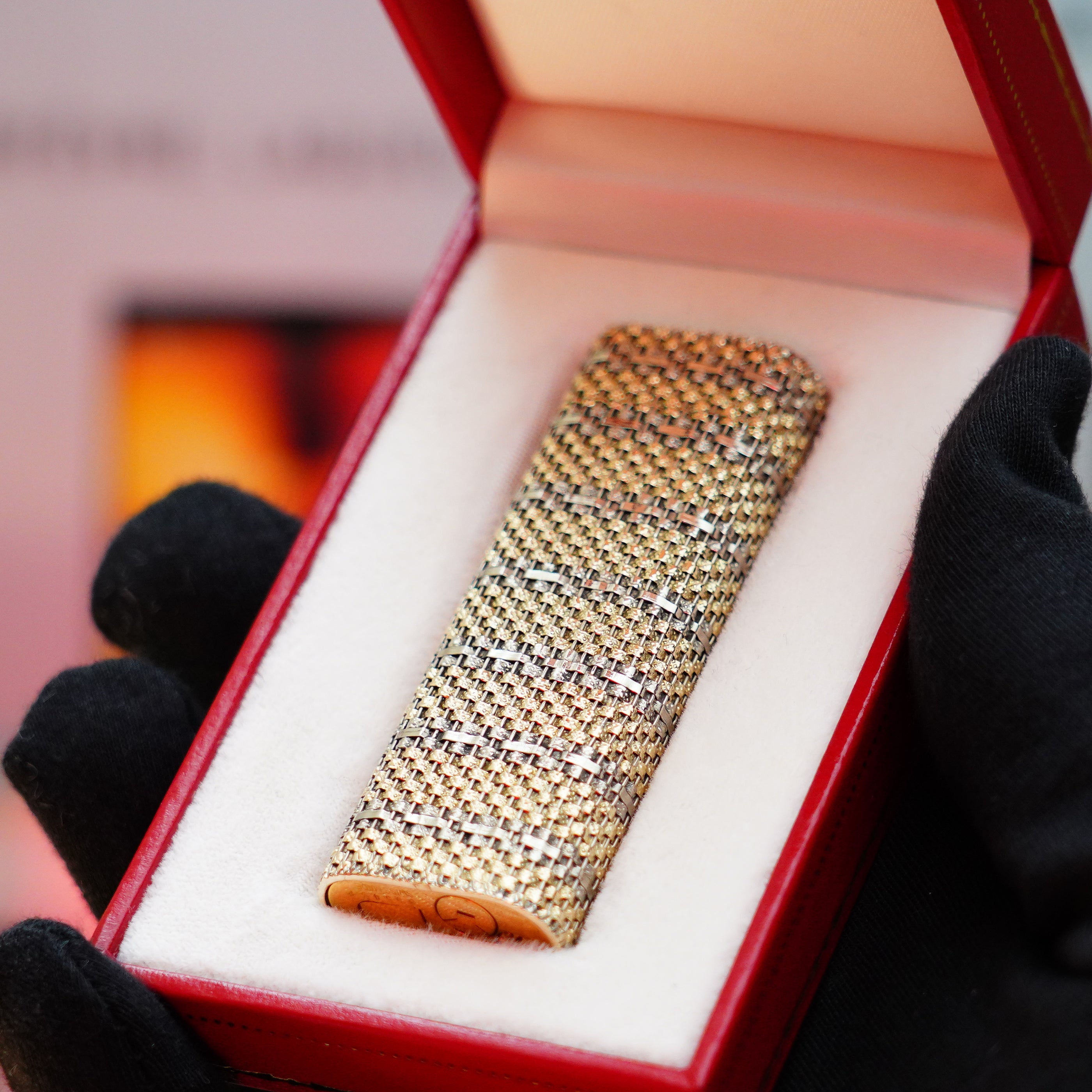 A Vintage 1982 Cartier Solid 18k Gold Jacket Basket Lighter, featuring the 750 hallmarks, is showcased inside an open red and white case, carefully held by gloved hands—a truly rare collectible.