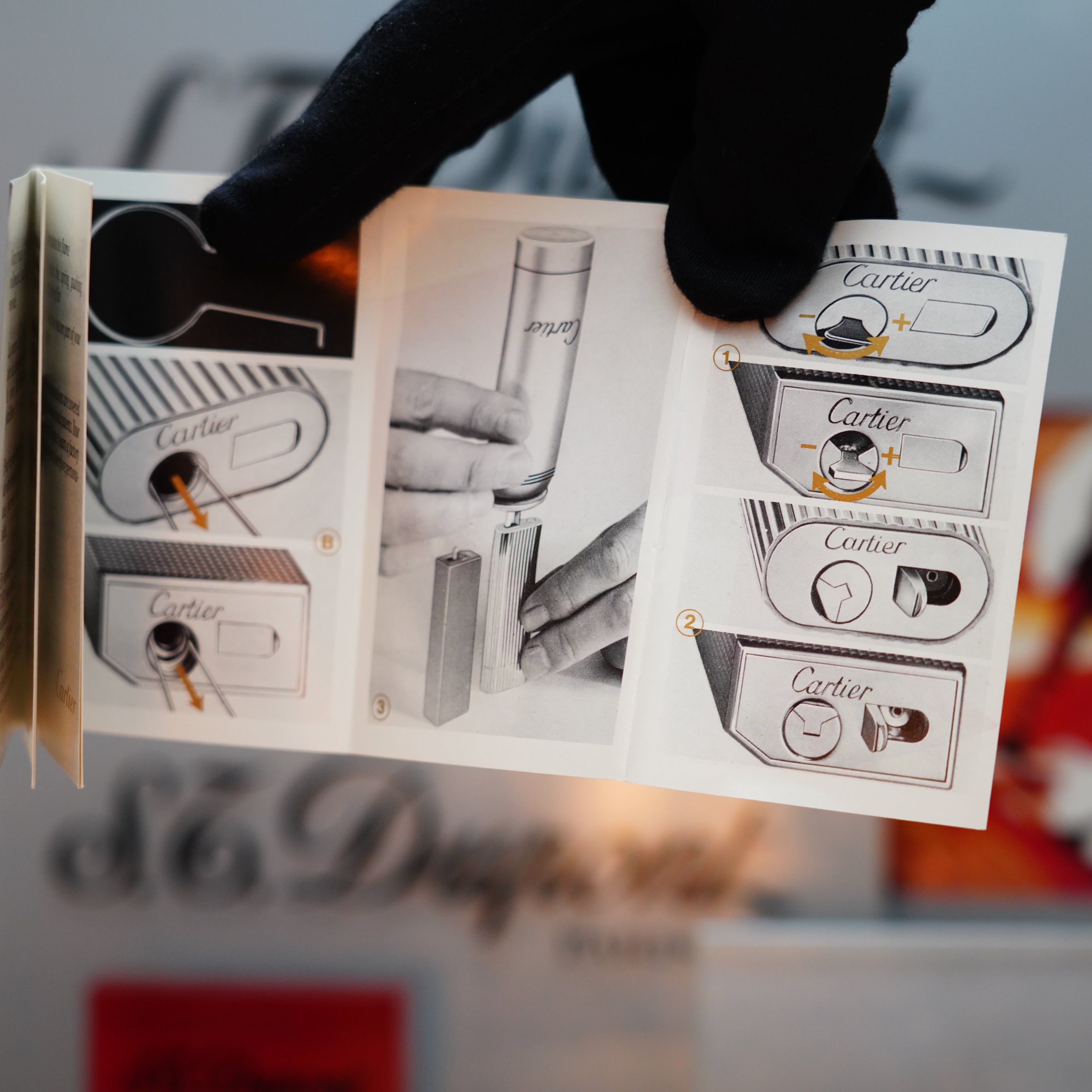 A black-gloved hand holds a booklet detailing the use and refilling of a rare mini-sized luxury lighter, featuring diagrams and text. This unique accessory showcases the elegance of the vintage 1982 Cartier Santos Pentagon design, crafted with palladium and solid 18k gold screws.