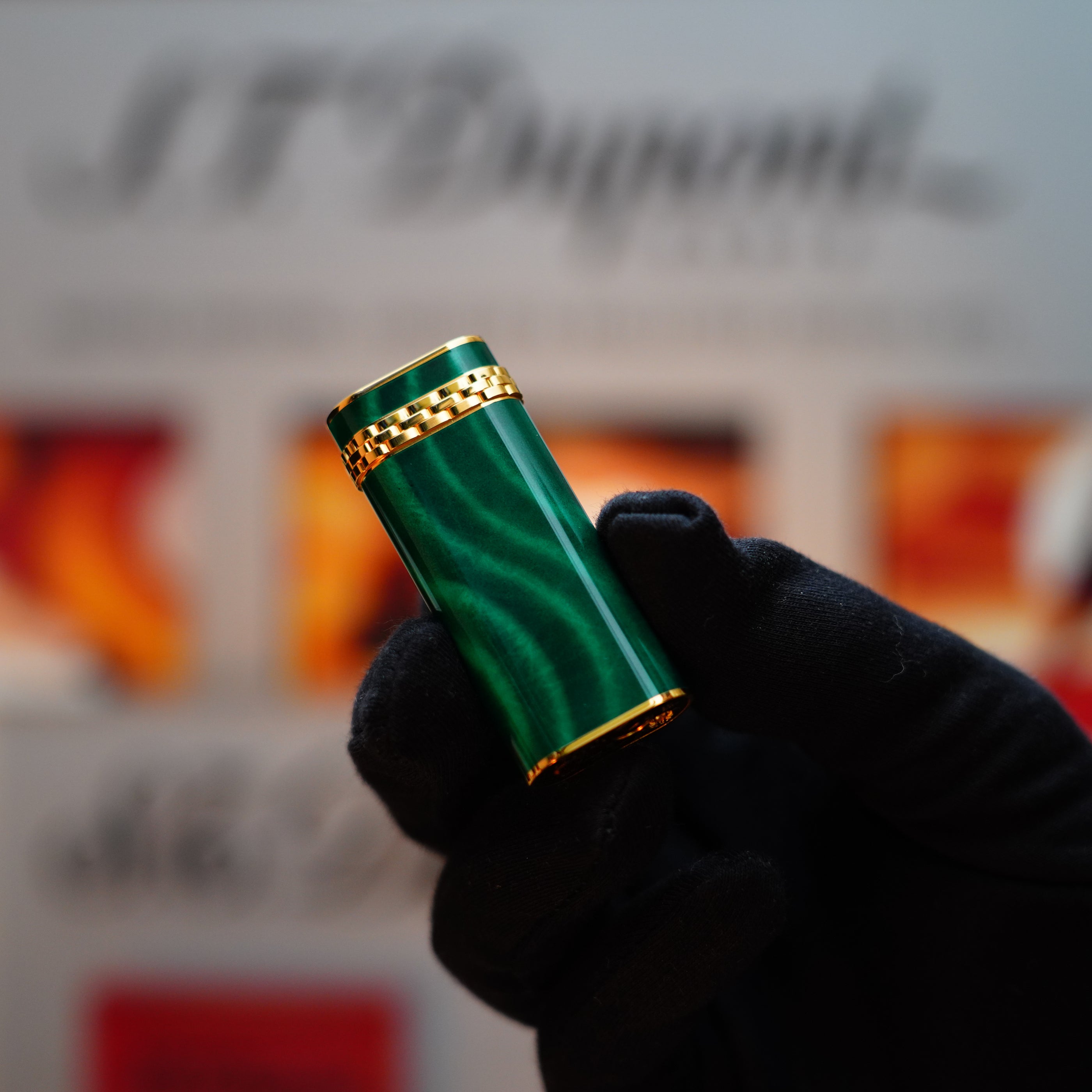 A gloved hand holds a vintage 1989 Cartier lighter, showcasing a luxurious 24k gold finish and a rare lacquer malachite gemstone design, complete with an elegant 18k gold ring on the door.