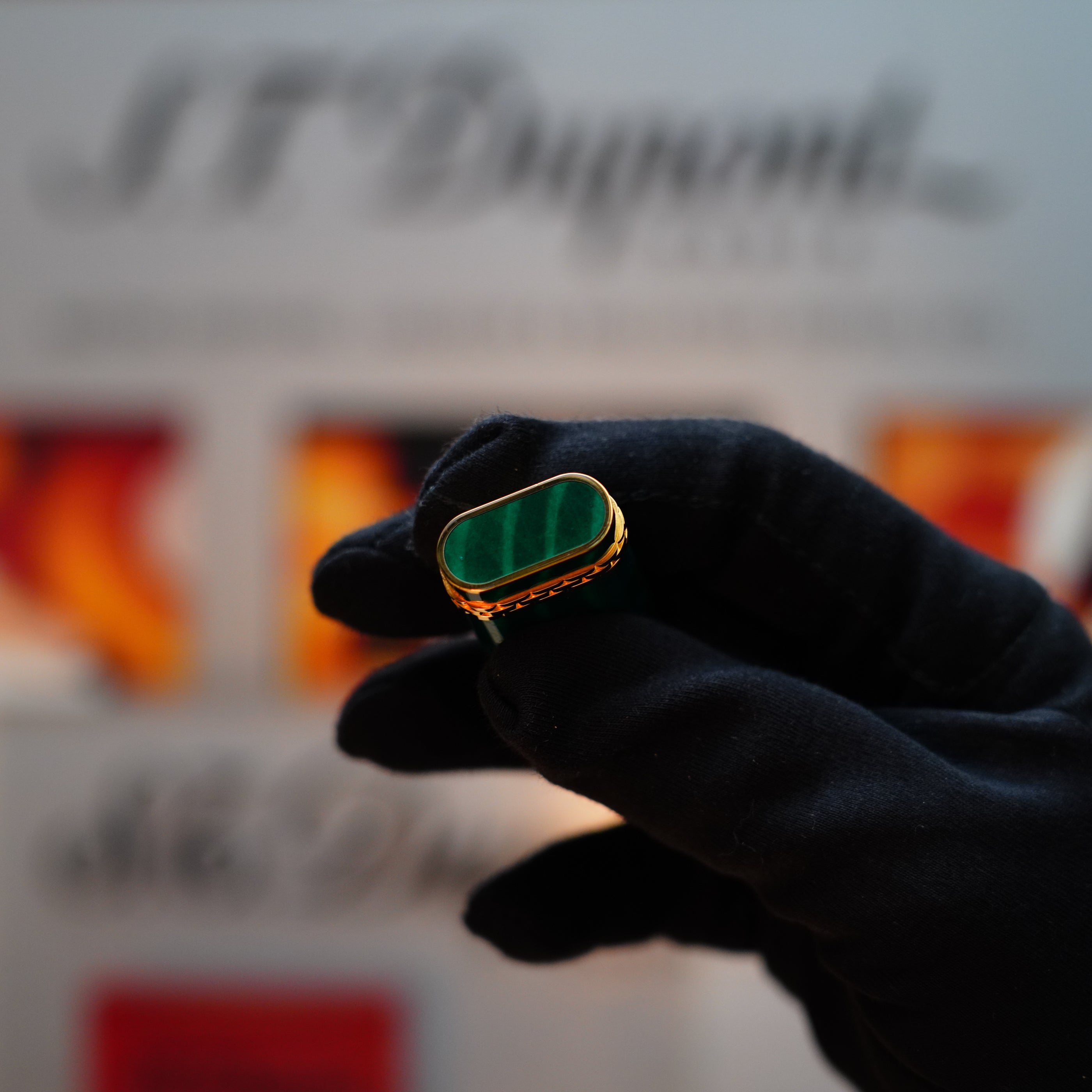 A gloved hand holds the exquisite Vintage 1989 Cartier Door Lighter, featuring a rare lacquer malachite gemstone mini and an 18k gold ring, set against a softly blurred background, evoking timeless elegance.