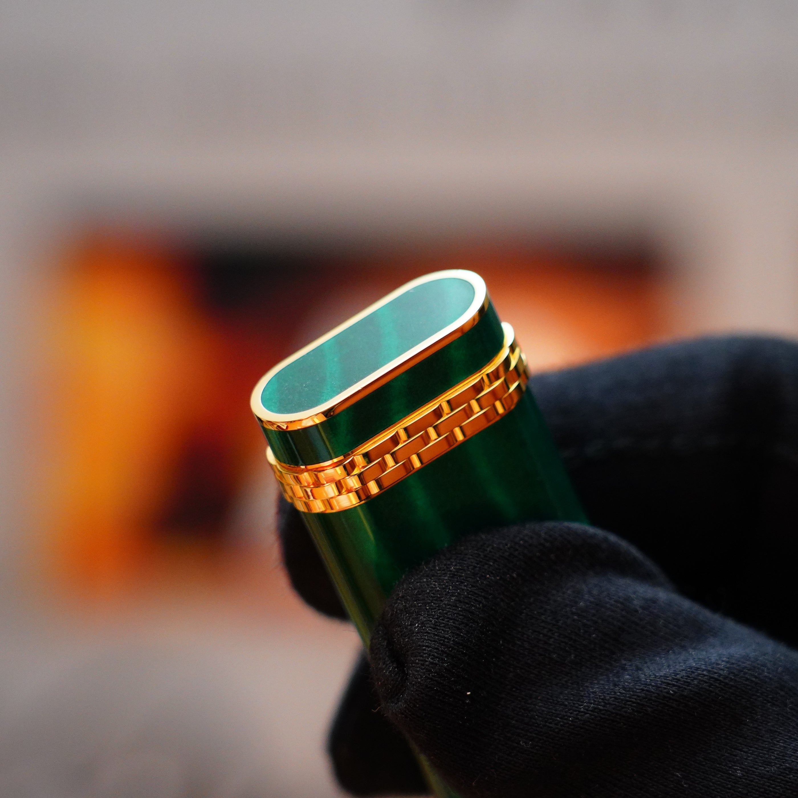 A gloved hand holds a Vintage 1989 Cartier lighter featuring a rare lacquer finish, its shiny surface reminiscent of the elegance of an 18k Gold Ring and the deep hues characteristic of a Malachite gemstone.