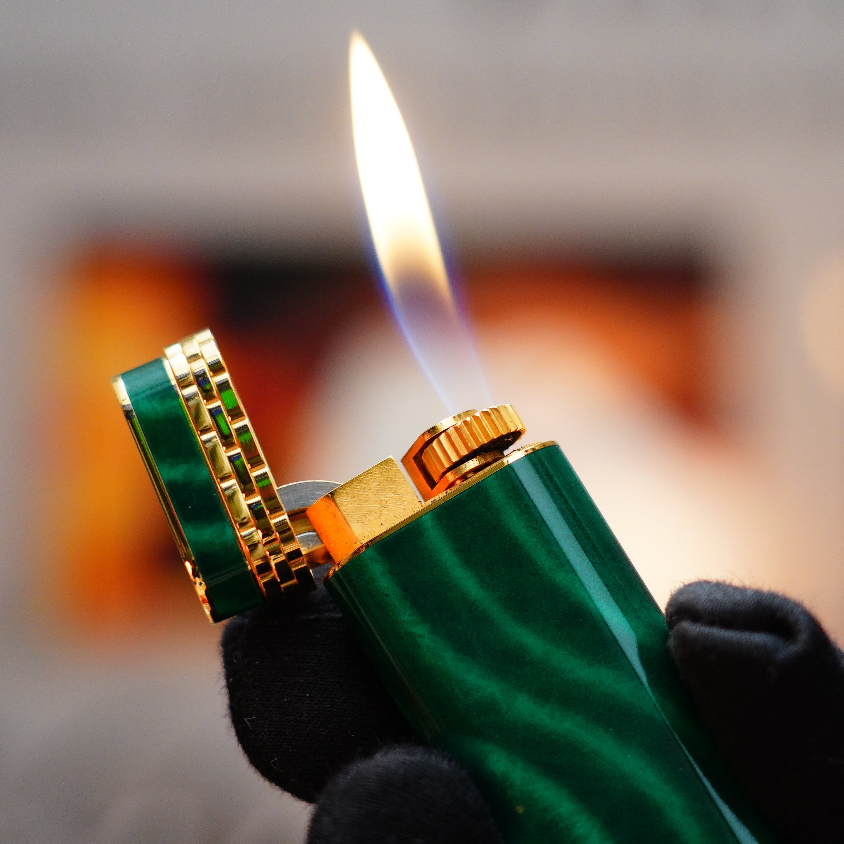 A gloved hand holds a Vintage 1989 Cartier lighter, its 24k gold finish and malachite gemstone accents sparkling alongside an open flame, with its exquisite design including an 18k gold ring on the door.