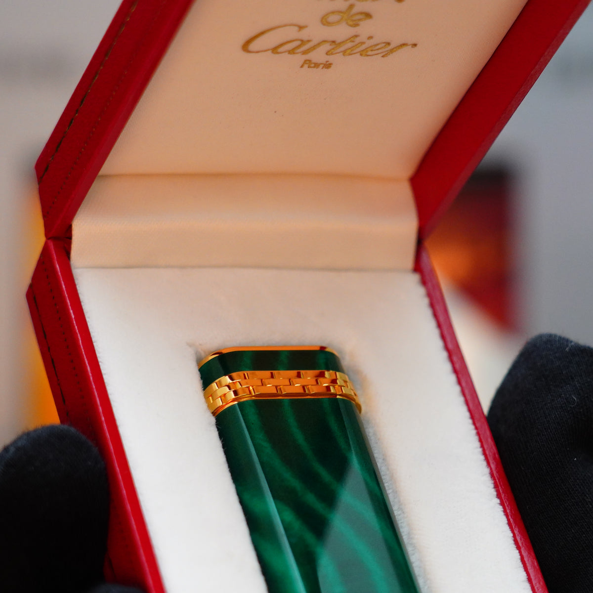 The Vintage 1989 Cartier lighter, featuring a rare lacquer malachite gemstone mini with a 24k gold finish and an 18k gold ring on the door, is elegantly presented in a striking red box.