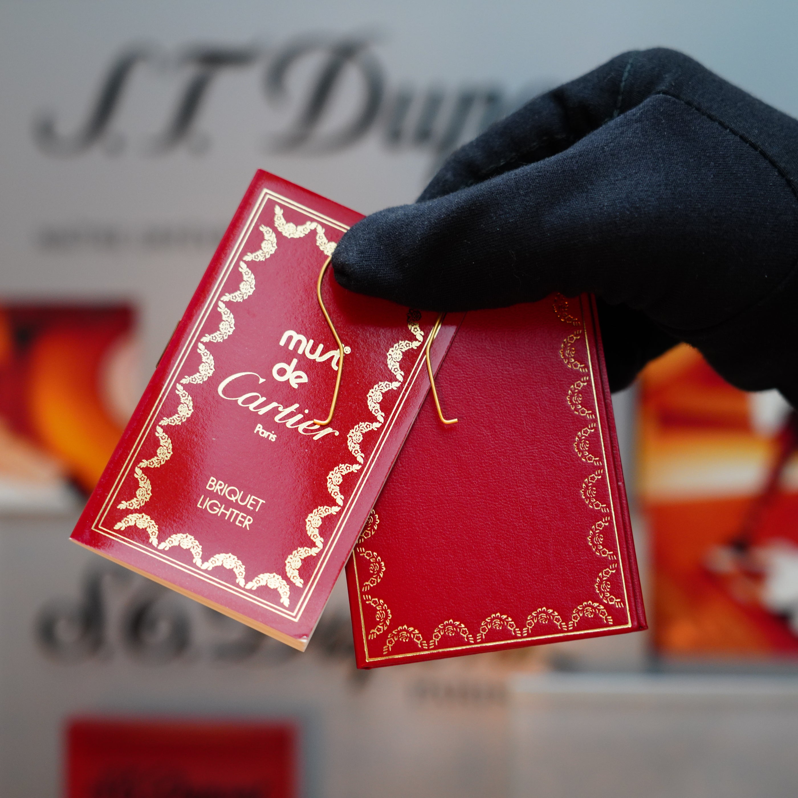 A gloved hand holds a red tag embossed with "Vintage 1989 Cartier 24k Gold Finish Rare Lacquer Malachite Gemstone Mini with 18k Gold Ring on Door Lighter" in gold lettering, embellished with a decorative border. The softly blurred background features iconic Cartier branding, appealing to those who cherish luxury akin to an exquisite 18k gold ring or malachite gemstone.