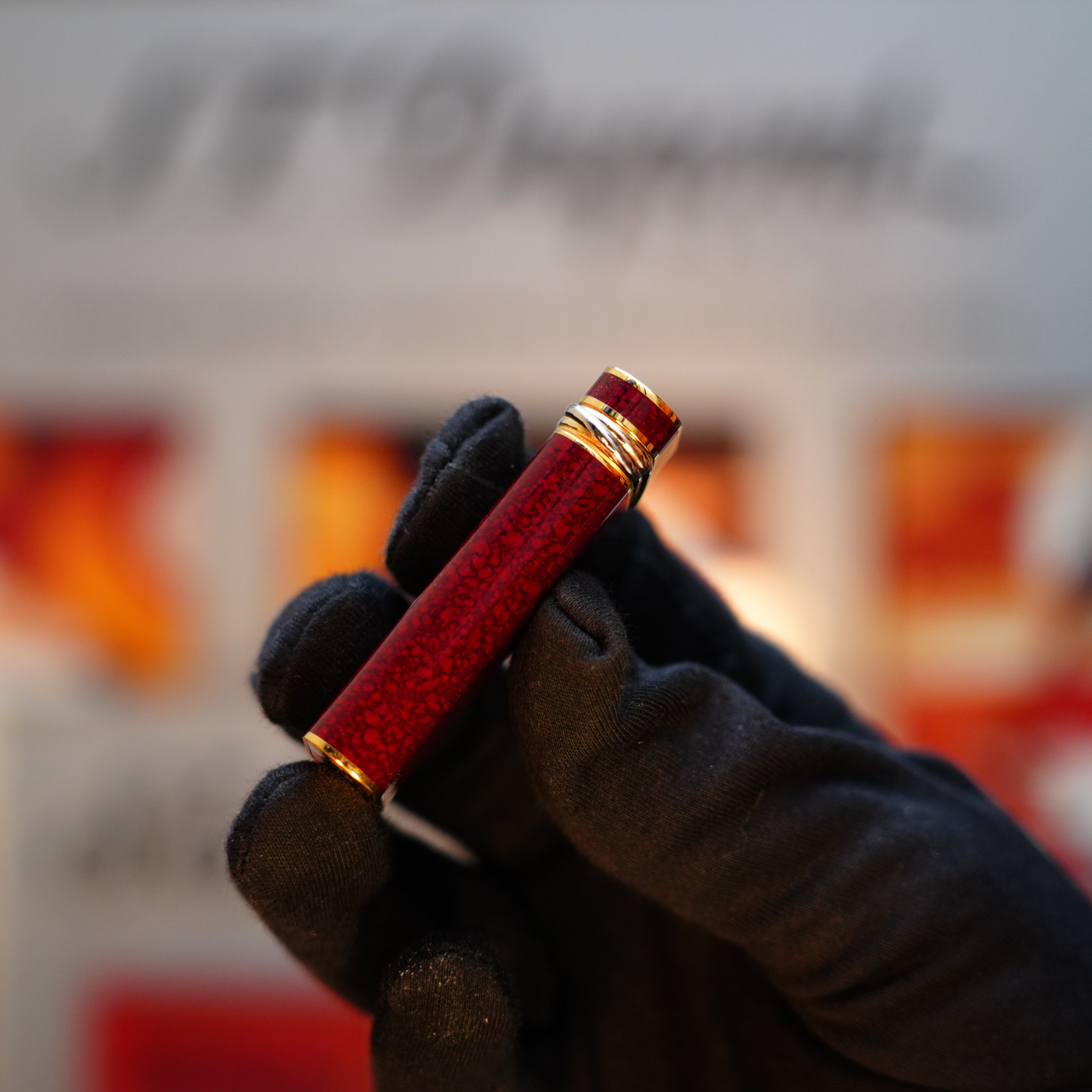 A gloved hand holds the Vintage 1989 Cartier 24k Gold Finish Rare Lacquer Jasper Gemstone Mini Lighter with an 18k Trinity Ring on the door, set against a blurred background.