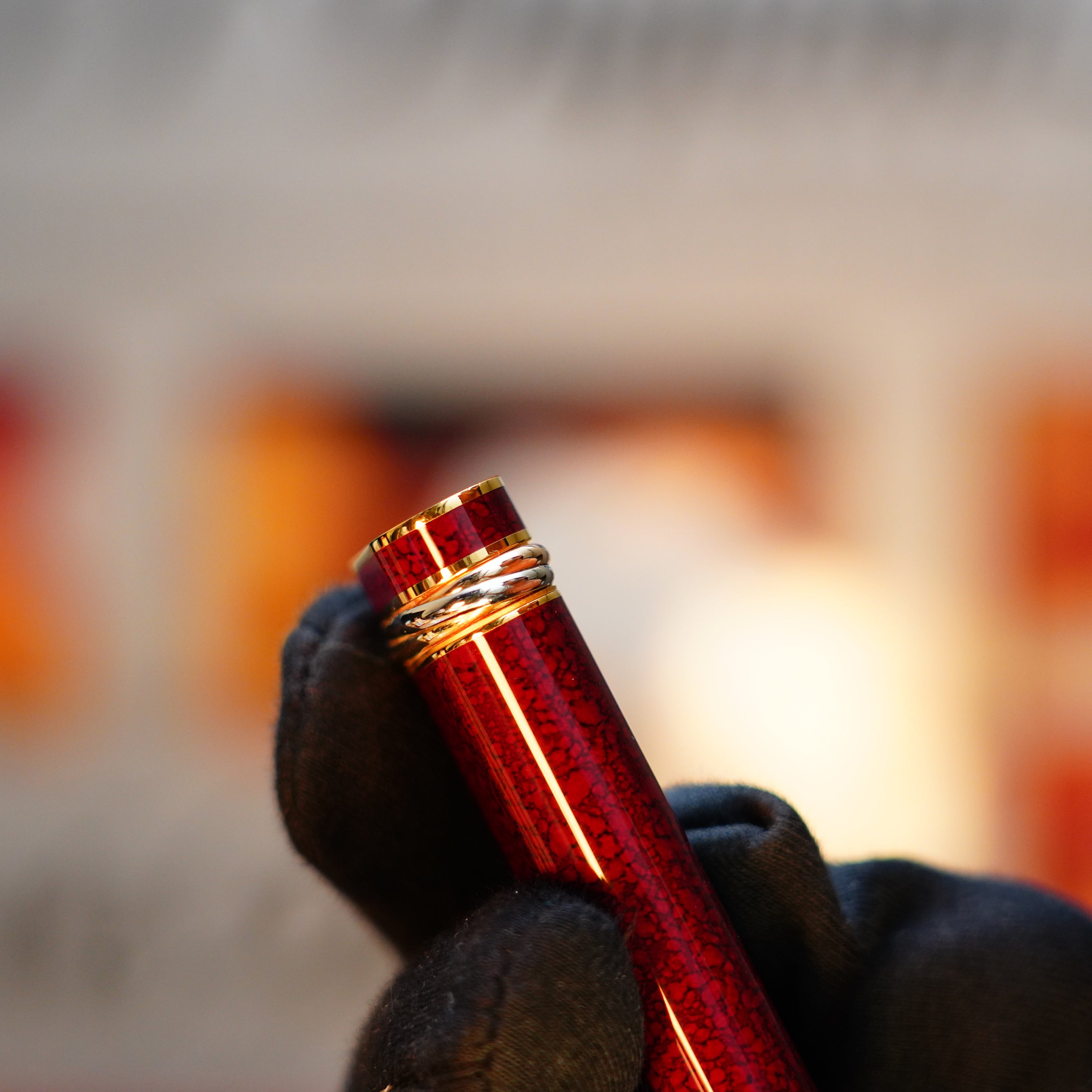 A gloved hand holds a red pen featuring a textured surface and gold accents, evoking the elegance of a Vintage 1989 Cartier 24k Gold Finish Lighter with Lacquer and Jasper Gemstone details. The background is softly blurred.