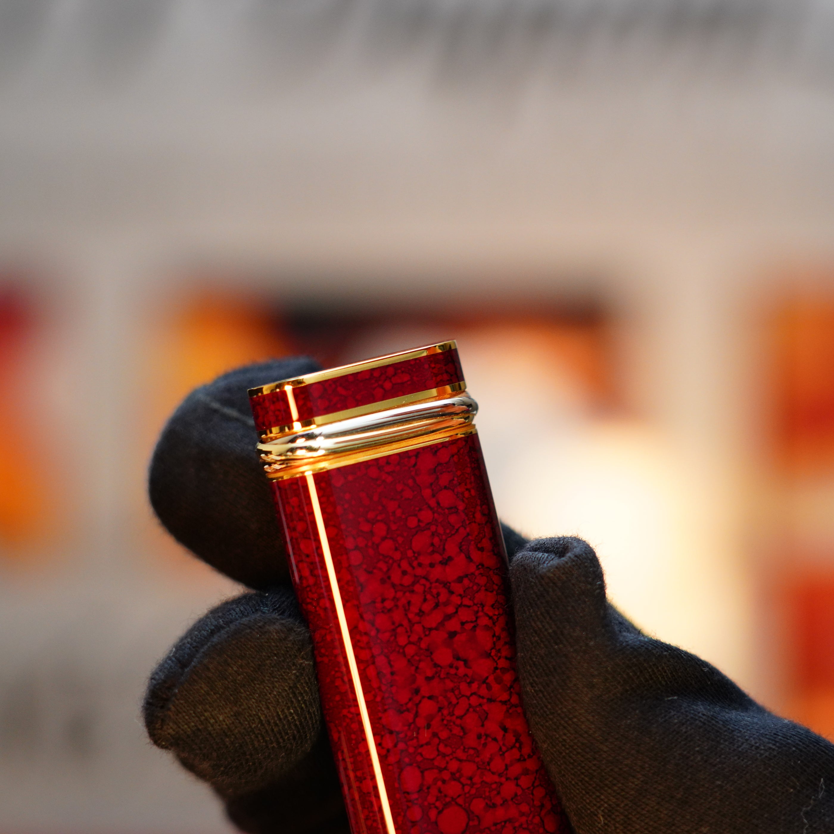 A gloved hand holds a red square bottle with a textured surface, reminiscent of the Vintage 1989 Cartier Jasper Gemstone Mini, adorned with an intricate silver wire around the neck.