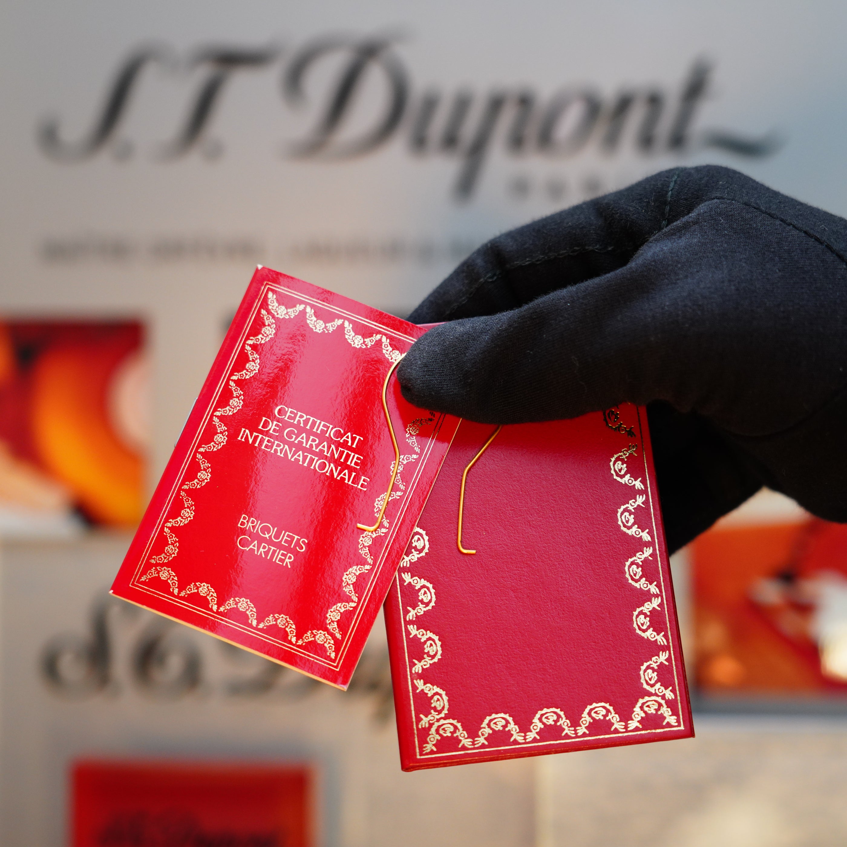 A gloved hand holds a red certificate with ornate borders, reminiscent of the elegance of the 18k Trinity Ring on a Vintage 1989 Cartier 24k Gold Finish Rare Lacquer Jasper Gemstone Mini Lighter, set against a blurred background.