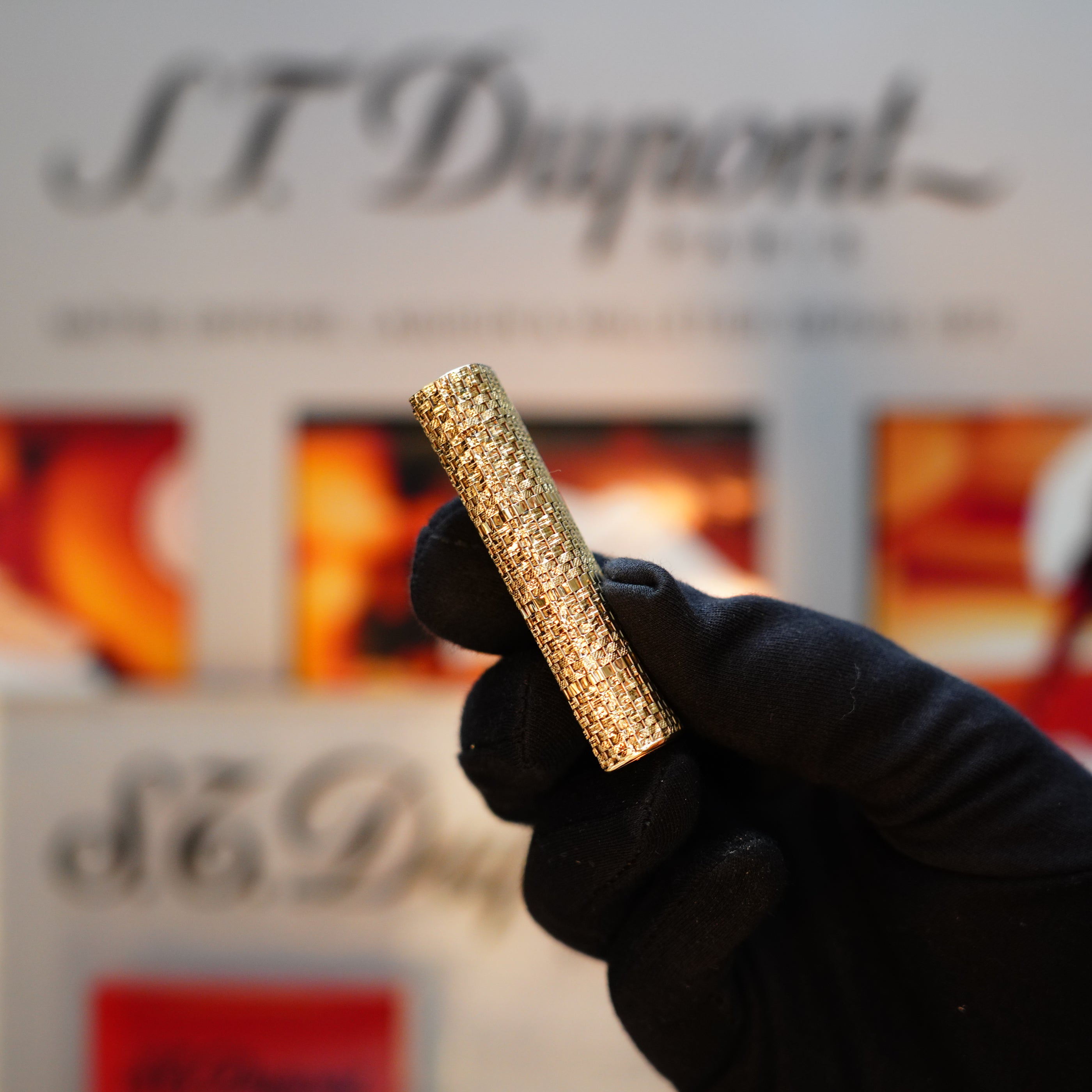 A gloved hand holds a textured gold lighter, echoing the signature basket design from Cartier's Vintage 1980 collection, with a blurred background showcasing the coveted display box.