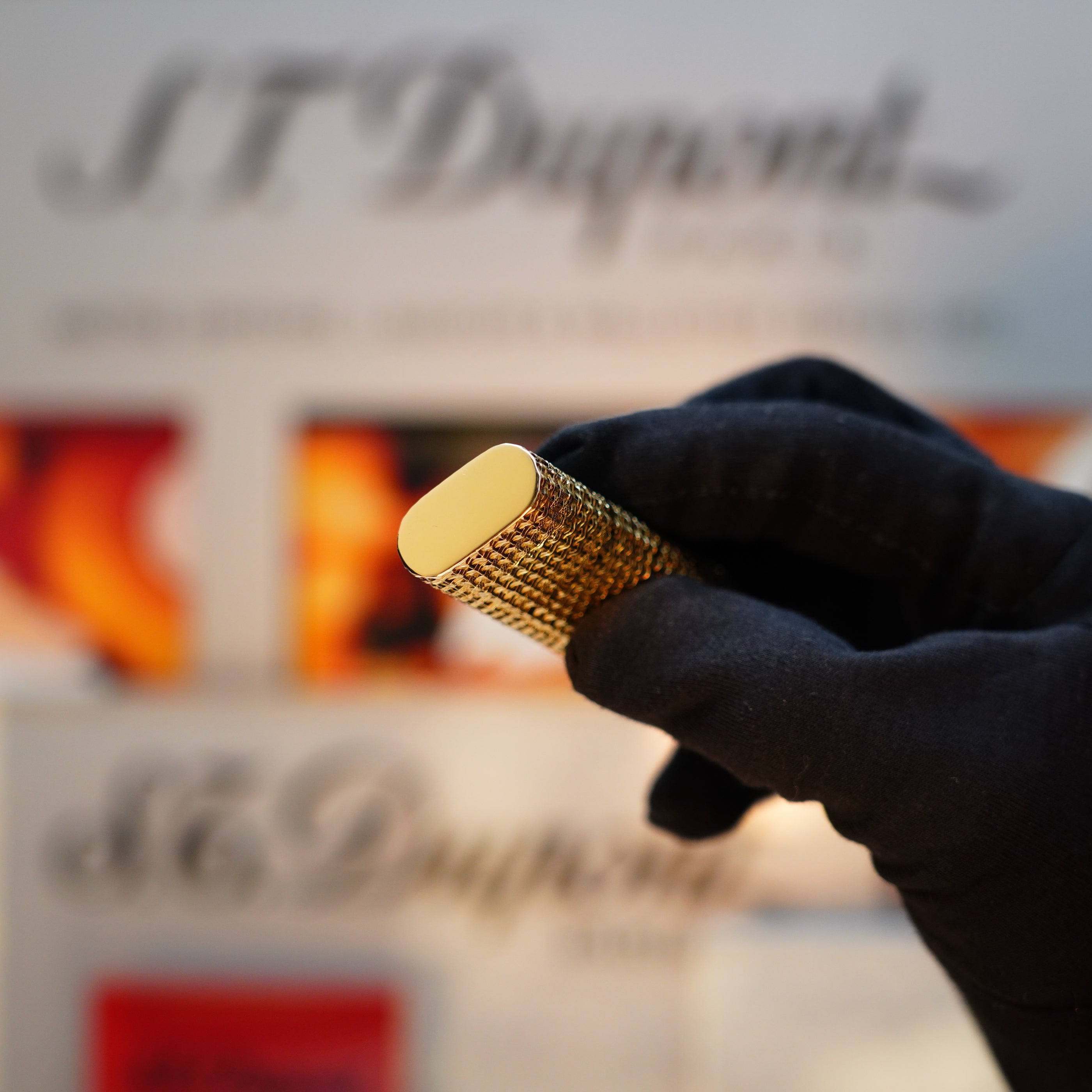 A gloved hand holds a Vintage 1980 Cartier Solid 18k Gold Jacket Basket lighter, marked with 750 hallmarks, while blurred branding by S.T. Dupont appears in the background.