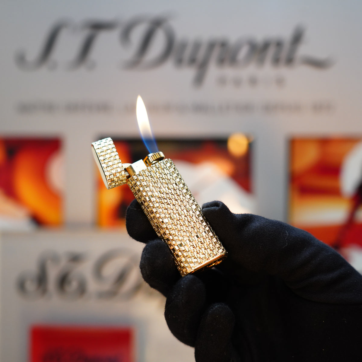 A gloved hand holds a lit, diamond-encrusted S.T. Dupont lighter against a blurred background, echoing the elegance of the Vintage 1980 Cartier Solid 18k Gold Jacket Basket Lighter, adorned with iconic 750 hallmarks and accompanied by its display box.