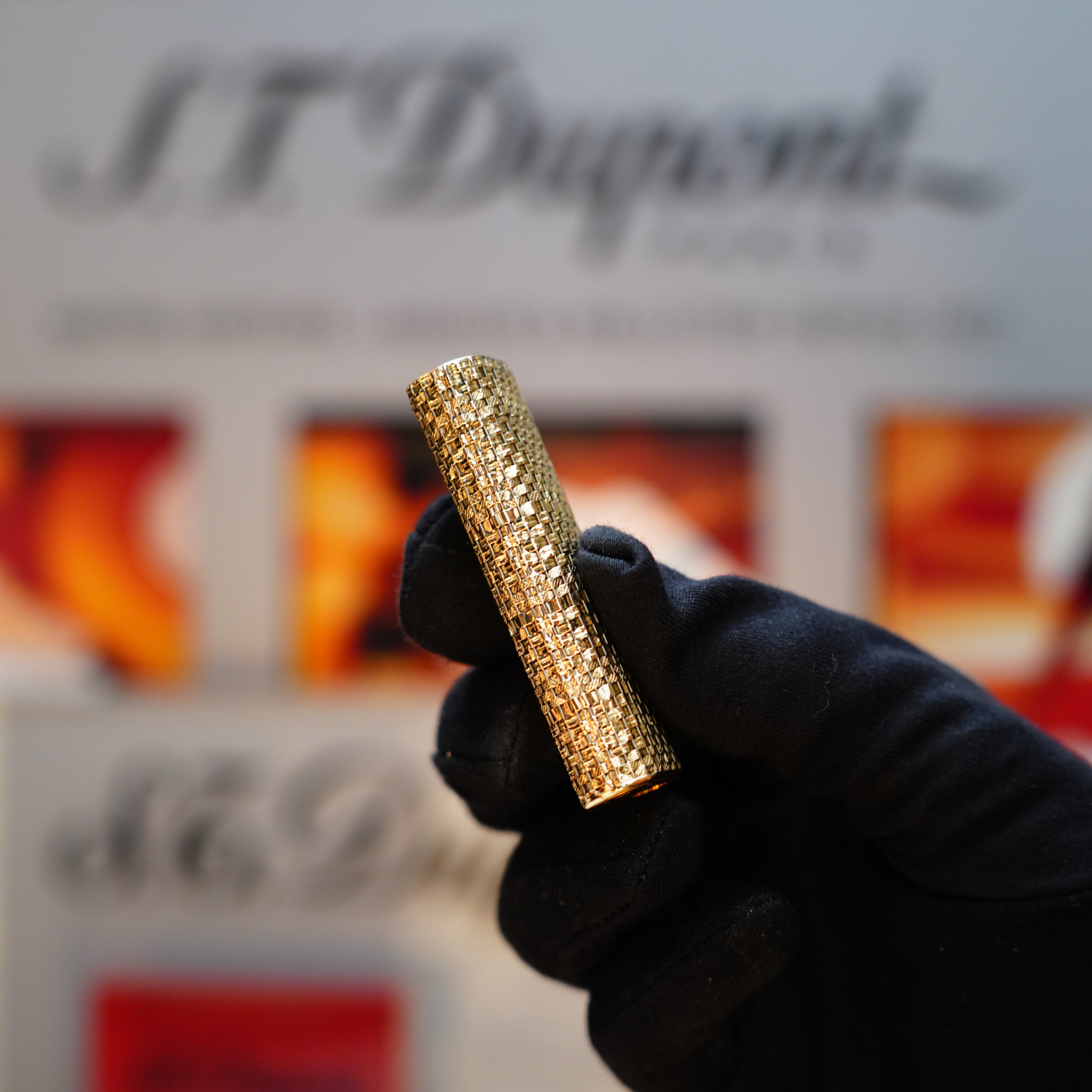 A gloved hand holds a textured, cylindrical gold object, likely a Vintage 1980 Cartier Solid 18k Gold Jacket Basket Lighter adorned with 750 hallmarks, set against a blurred background.