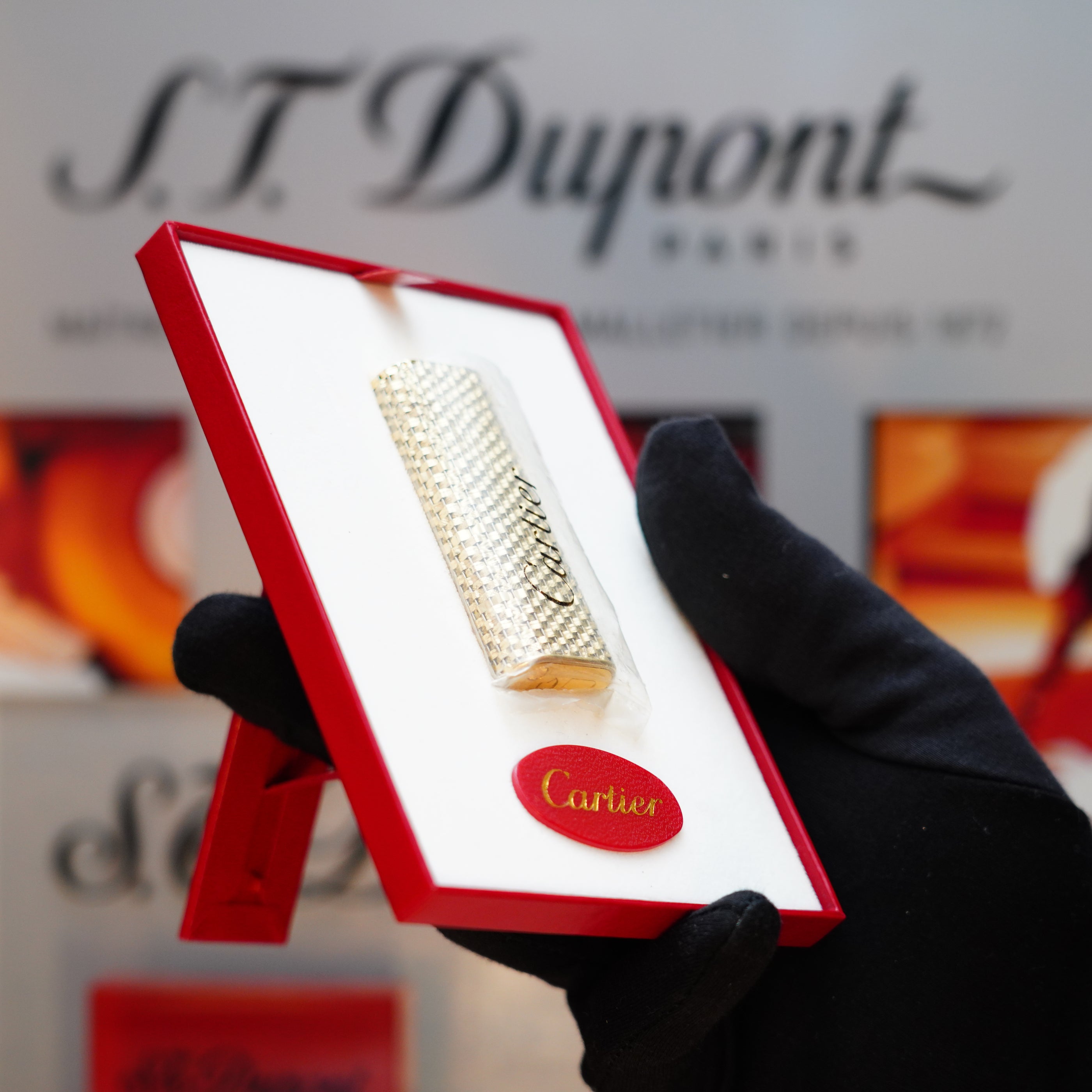 A gloved hand holds a red box, revealing a Vintage 1980 Cartier Solid 18k Gold Jacket Basket Lighter with 750 hallmarks, echoing the timeless elegance of Cartier.