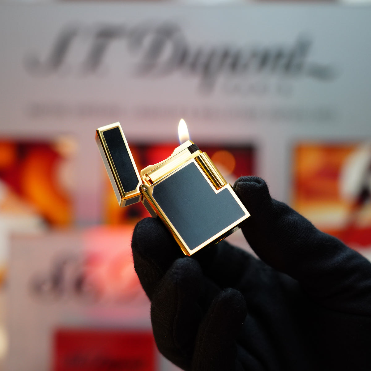 A gloved hand holds a vintage 1990 S.T. Dupont Noire Heavy 24k Gold Matt Black Lacquer Ligne 1 Lighter with a visible flame against a blurred background.