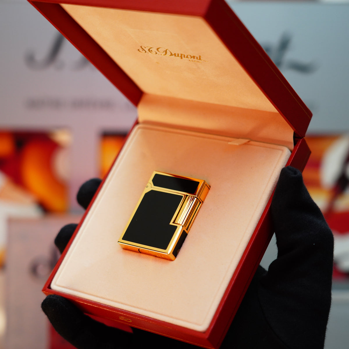 A gloved hand delicately holds an open red box revealing a Vintage 1990 St Dupont Noire Heavy 24k Gold Matt Black Lacquer Ligne 1 lighter by S.T. Dupont.