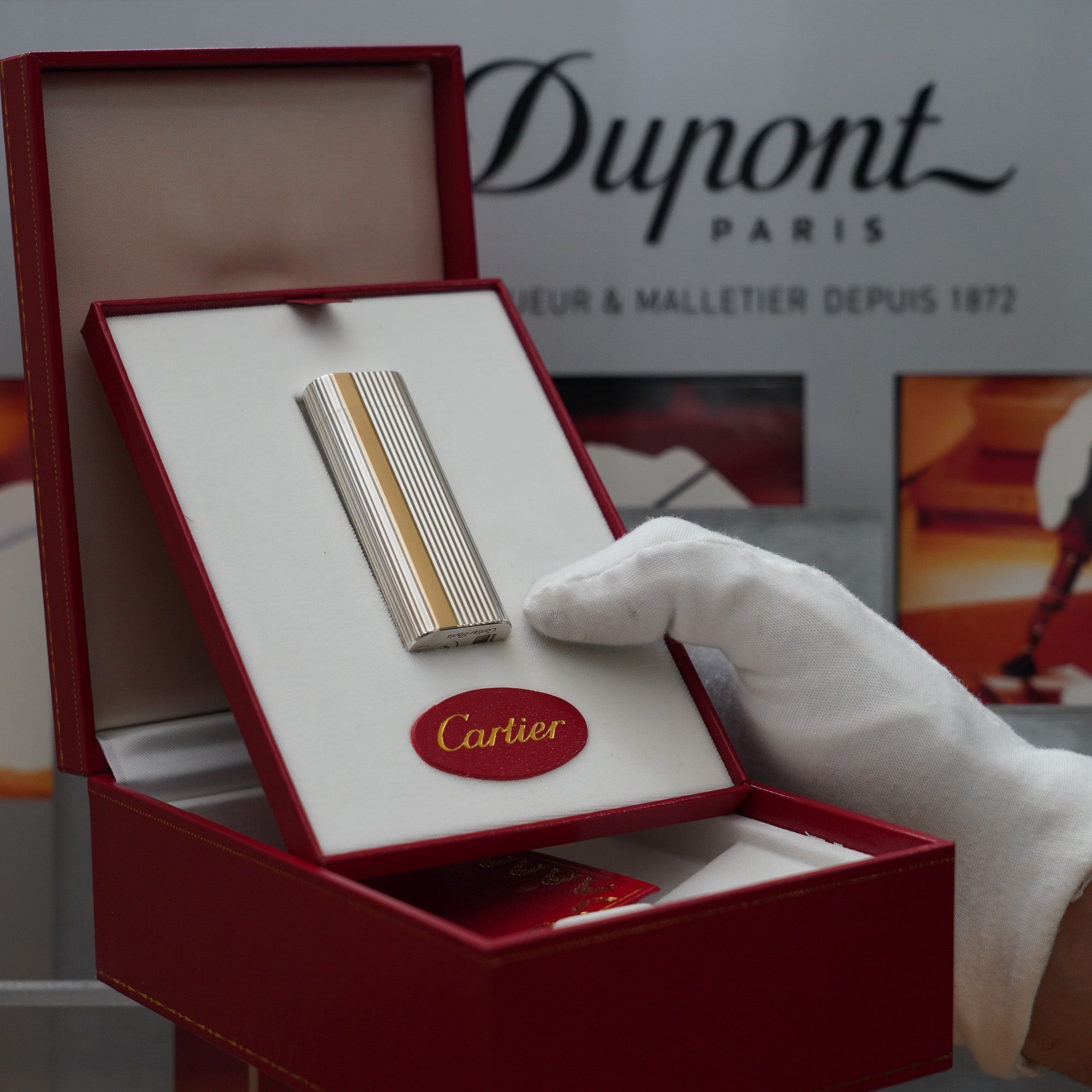 A person is holding a Vintage 1980 Cartier Solid Silver 925 & Gold 750 Lighter with 18k Solid Gold Strip Factory Made in a Dupont box.