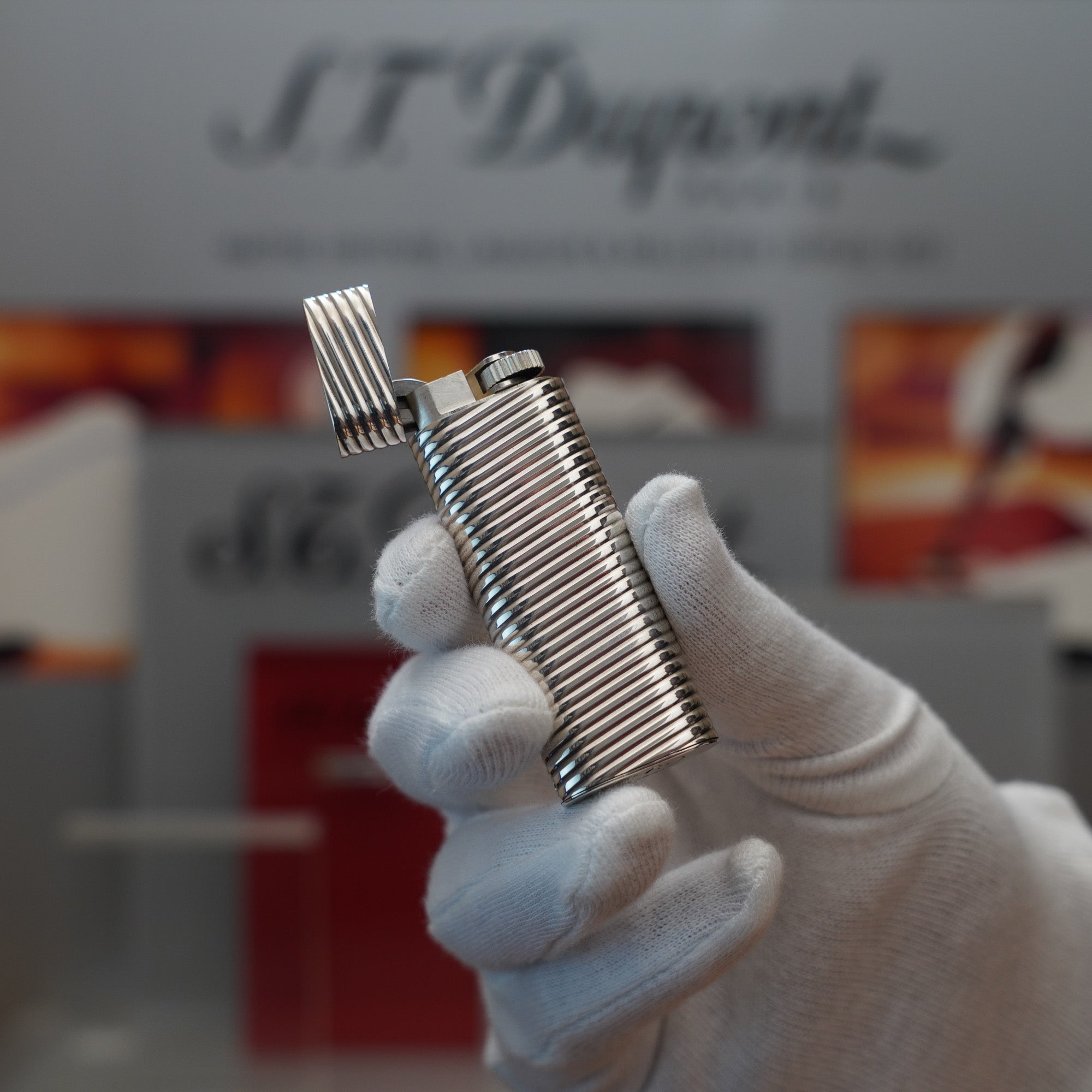 A person holding a Vintage 1980 Cartier Solid Silver 925 Lighter Factory Argent ( Torsade ) in front of a display.