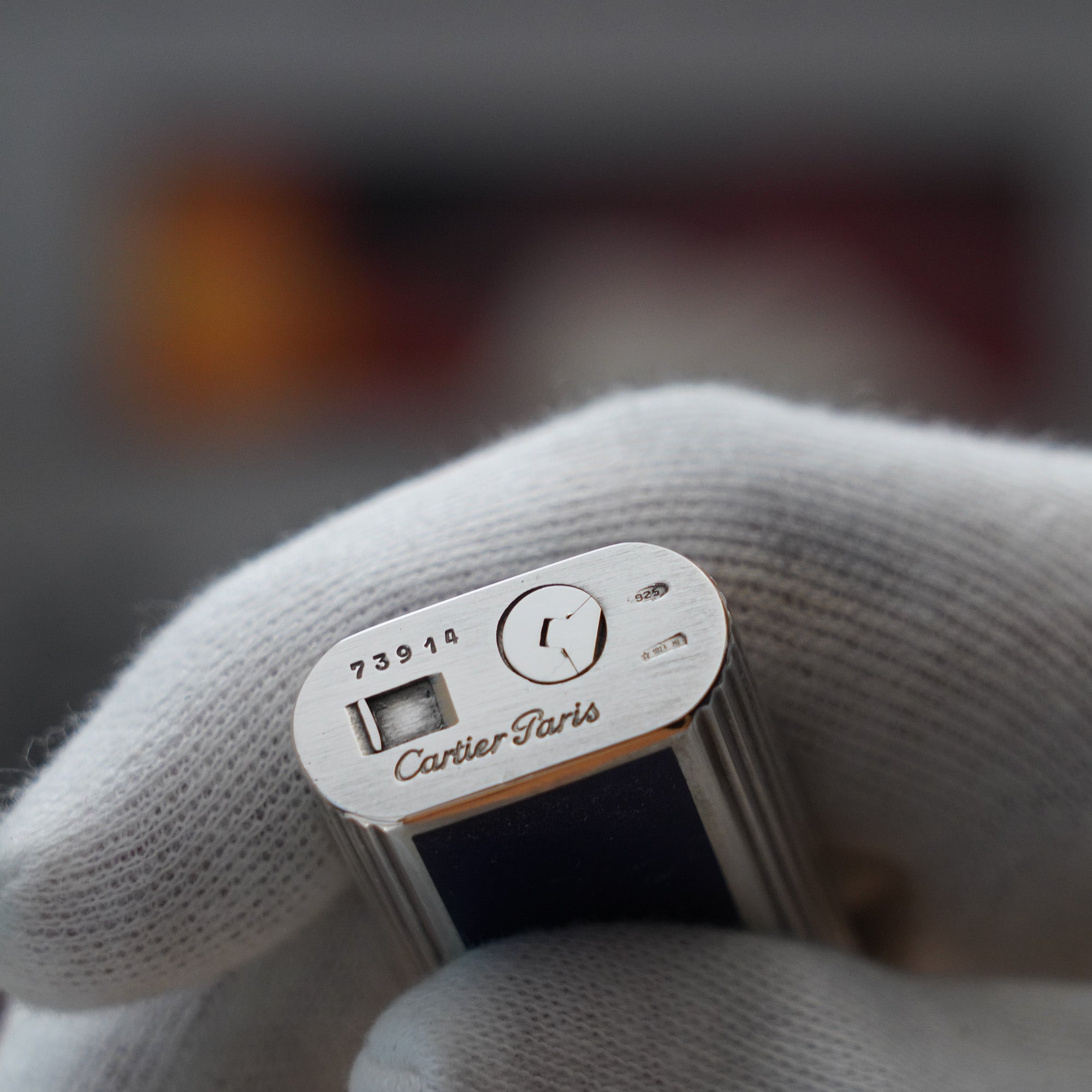 A Vintage 1980 Cartier Solid Silver 925 Blue Enamel Factory (Smalto Blu) lighter being held by a person's hand.