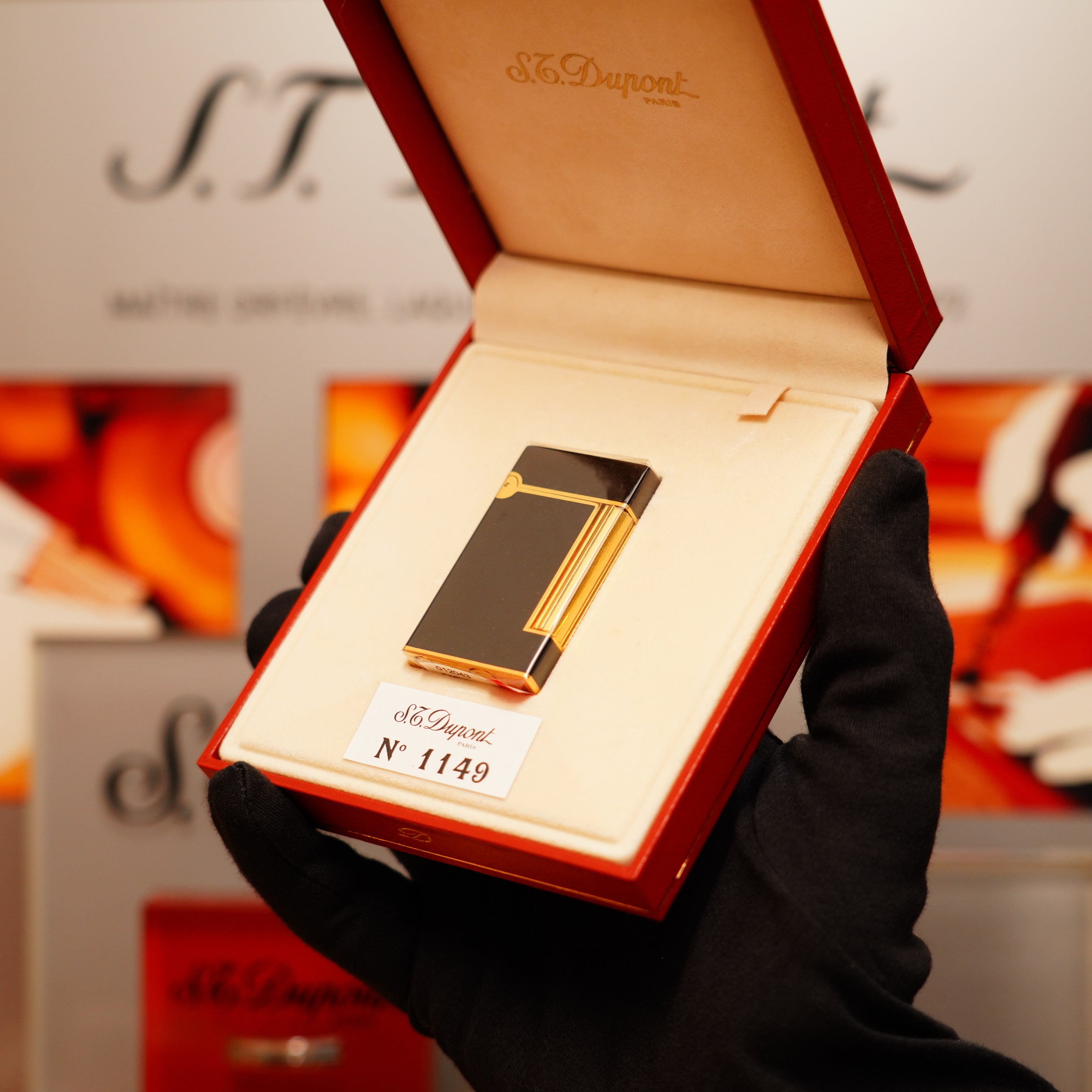 A gloved hand showcases a Vintage 1990 S.T. Dupont black lacquer and gold Ligne D lighter, elegantly displayed in an open red case.