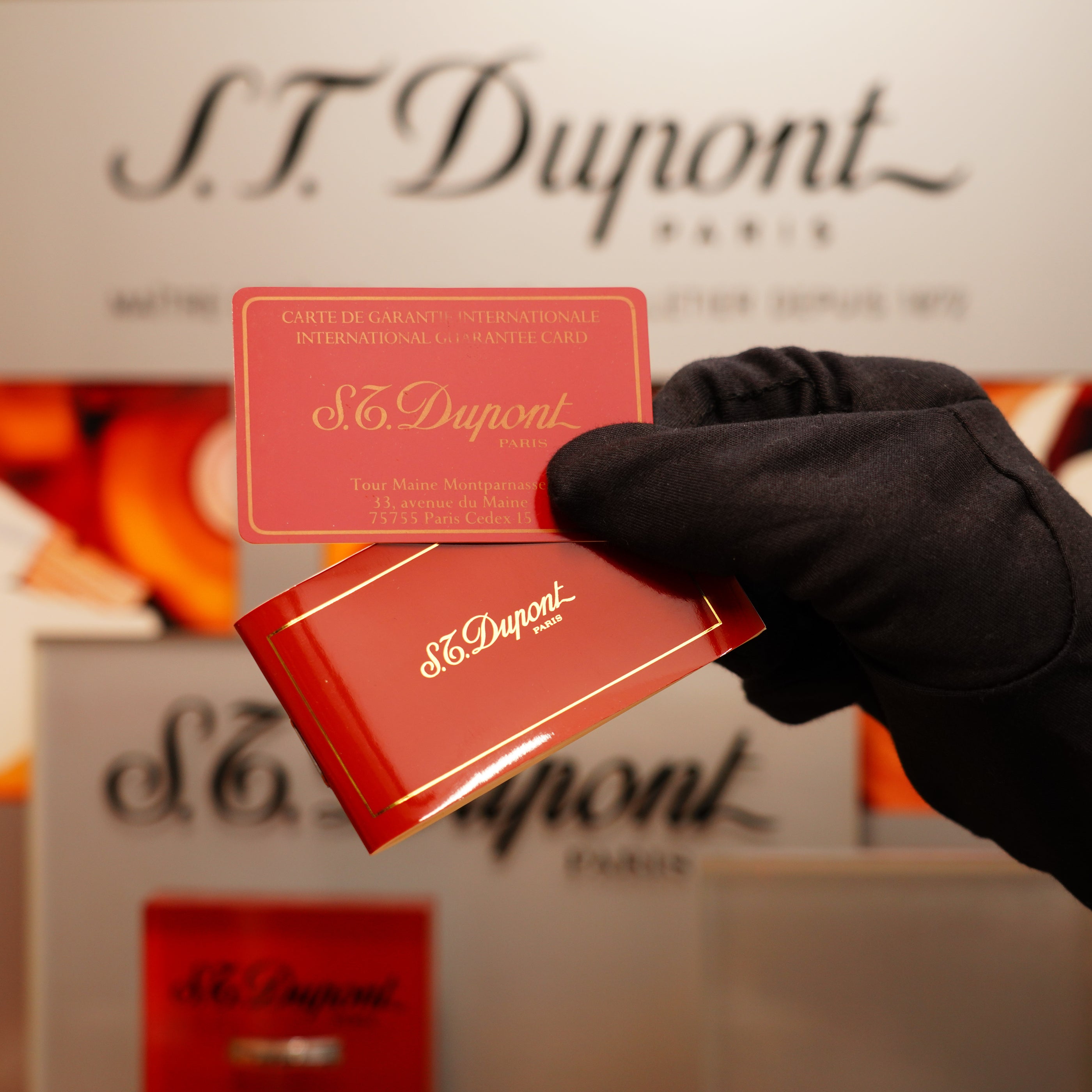 A gloved hand holds a red S.T. Dupont box and warranty card with the brand's logo displayed, featuring the Vintage 1990 St Dupont Overall Black Lacquer Early 24k Gold Ligne D Sealed Lighter.