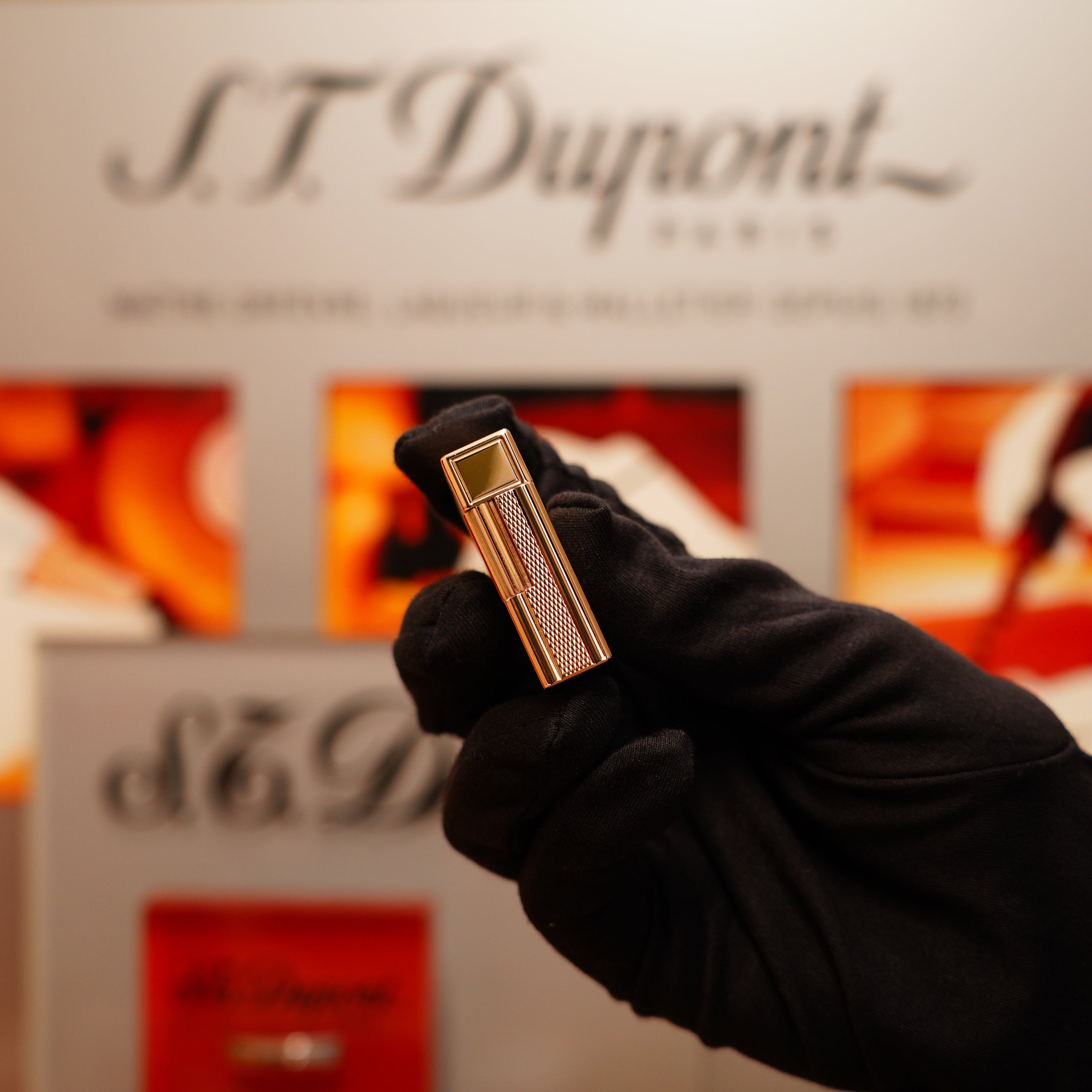 A gloved hand holds a Vintage 1990 S.T. Dupont 24k Gold Iconic Ligne 1 lighter with small dots and line pattern against a blurred background featuring the brand's signage.