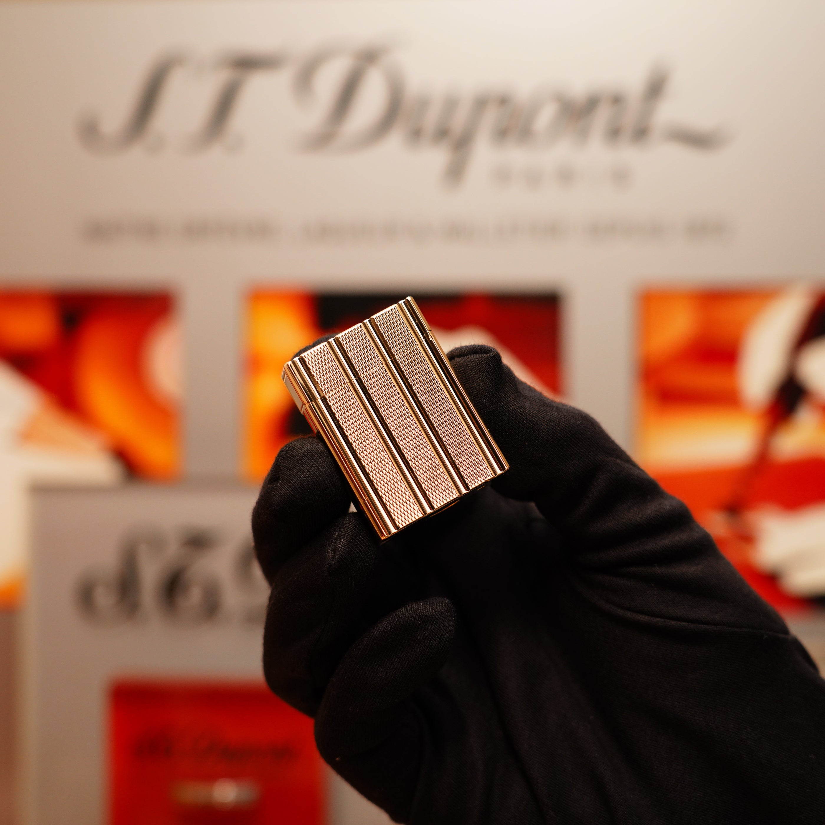 A gloved hand holds a Vintage 1990 S.T. Dupont 24k Gold Iconic Ligne 1 Small Dots and Line Pattern Lighter with the brand's logo visible in the blurred background.