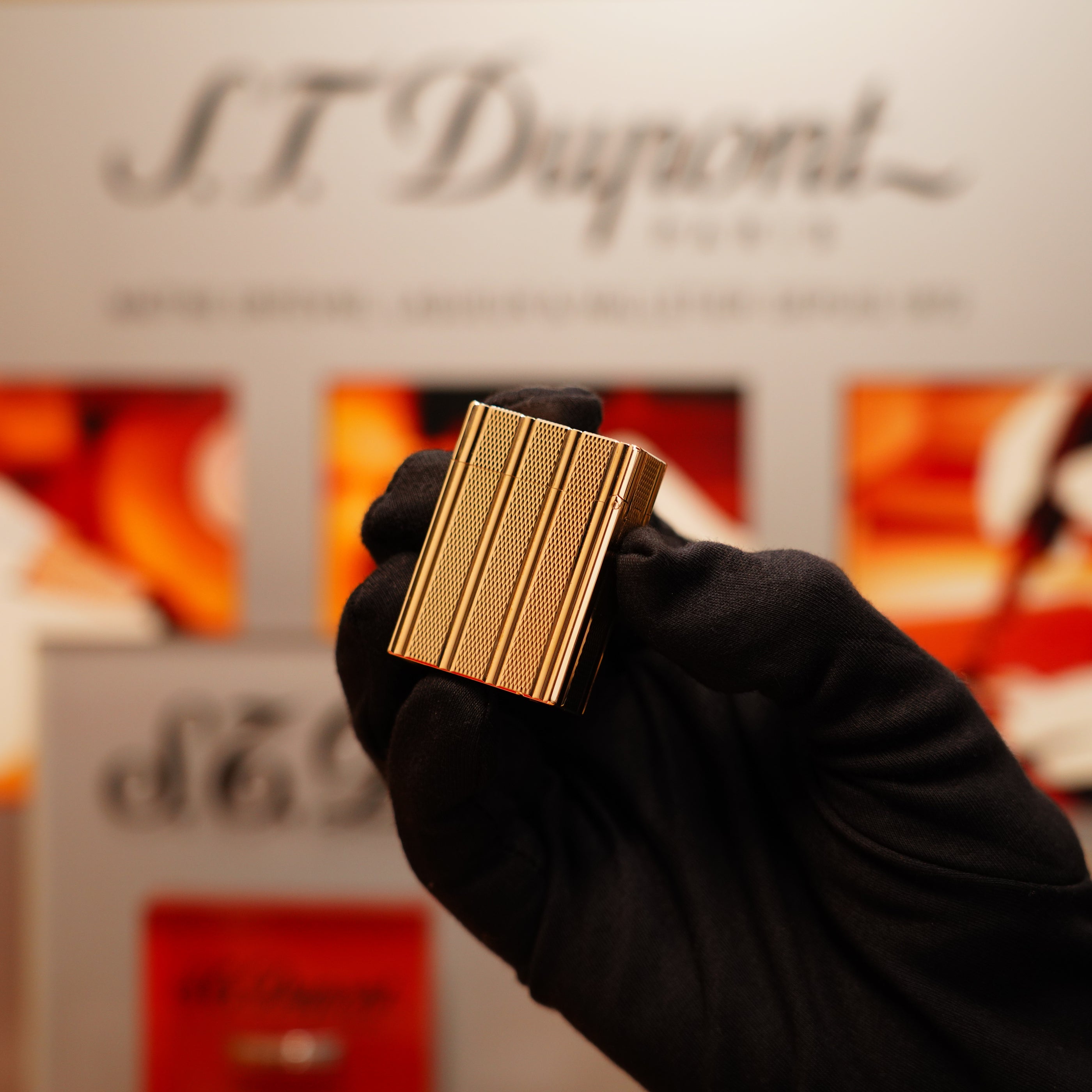 A black-gloved hand holds a Vintage 1990 S.T. Dupont 24k Gold Iconic Ligne 1 Small Dots and Line Pattern Lighter against an S.T. Dupont display background.