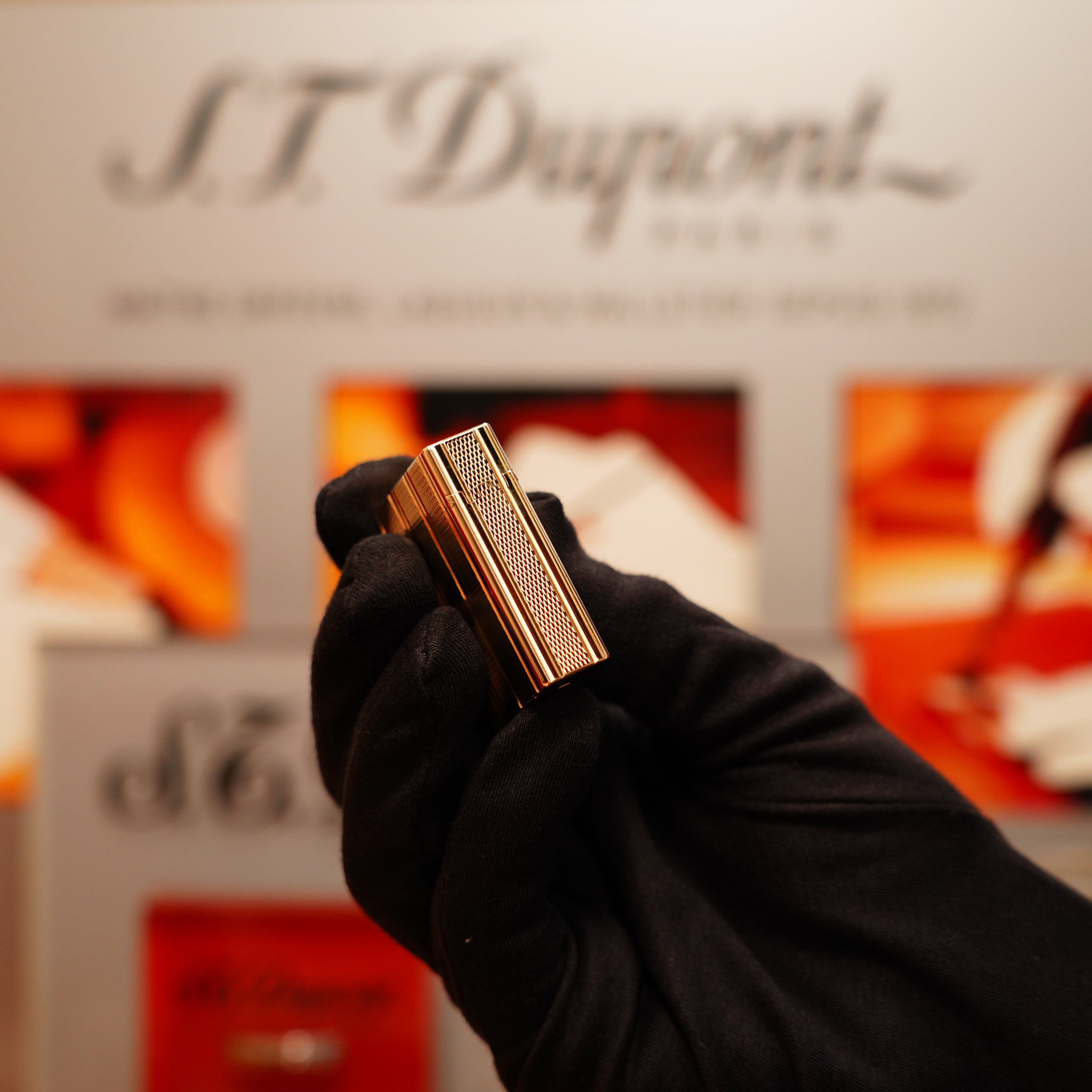 A gloved hand holds a Vintage 1990 S.T. Dupont 24k Gold Iconic Ligne 1 Lighter with a small dots and line pattern against a blurred background, featuring the text "S.T. Dupont.