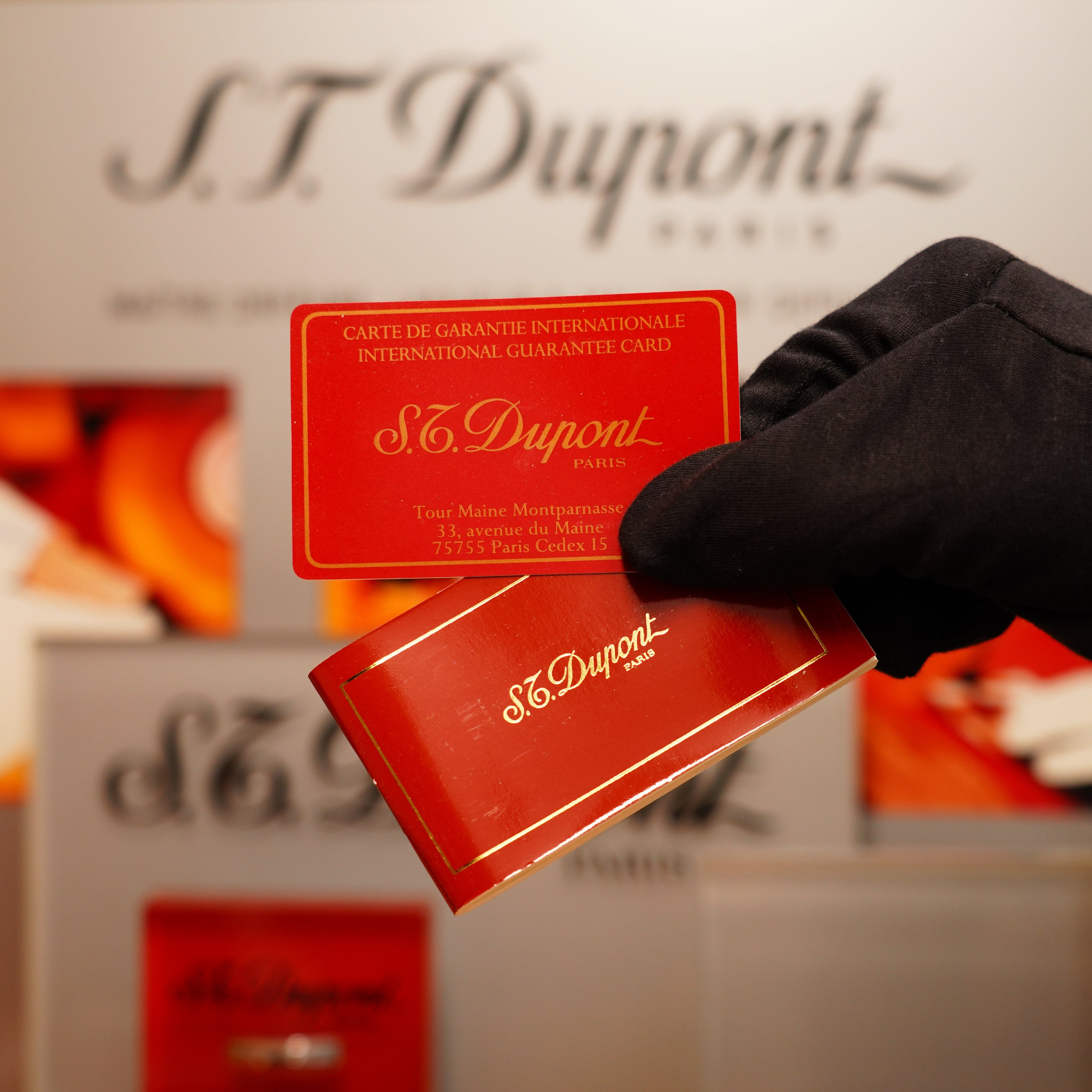 A gloved hand holds two red S.T. Dupont cards against a blurred backdrop featuring the S.T. Dupont logo.