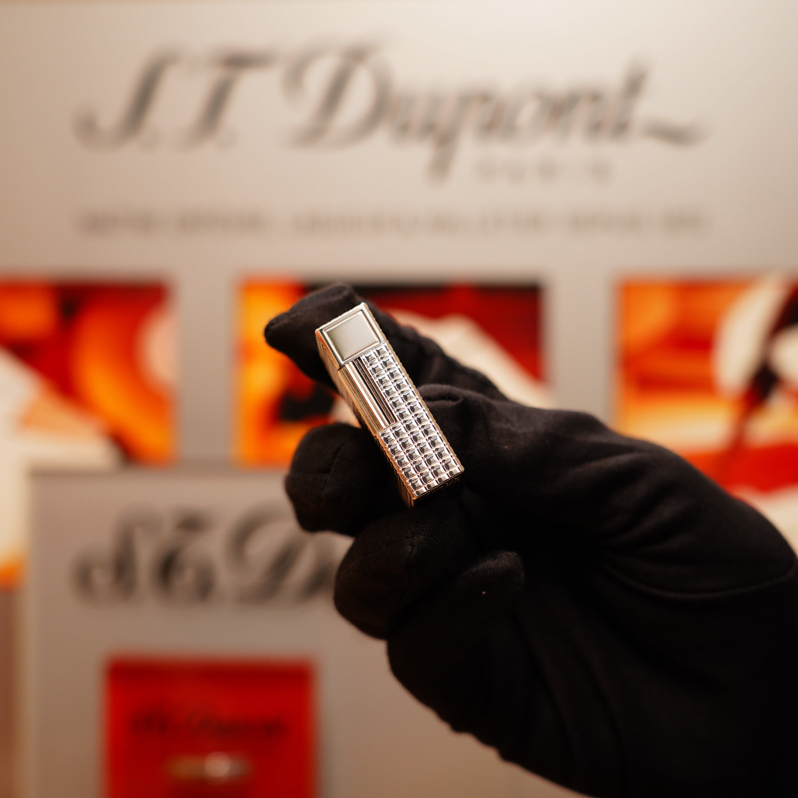 A gloved hand holds a Vintage 1990 S.T. Dupont Ligne 1 lighter with a rare window pattern and heavy silver finish, set against a blurred S.T. Dupont brand display.