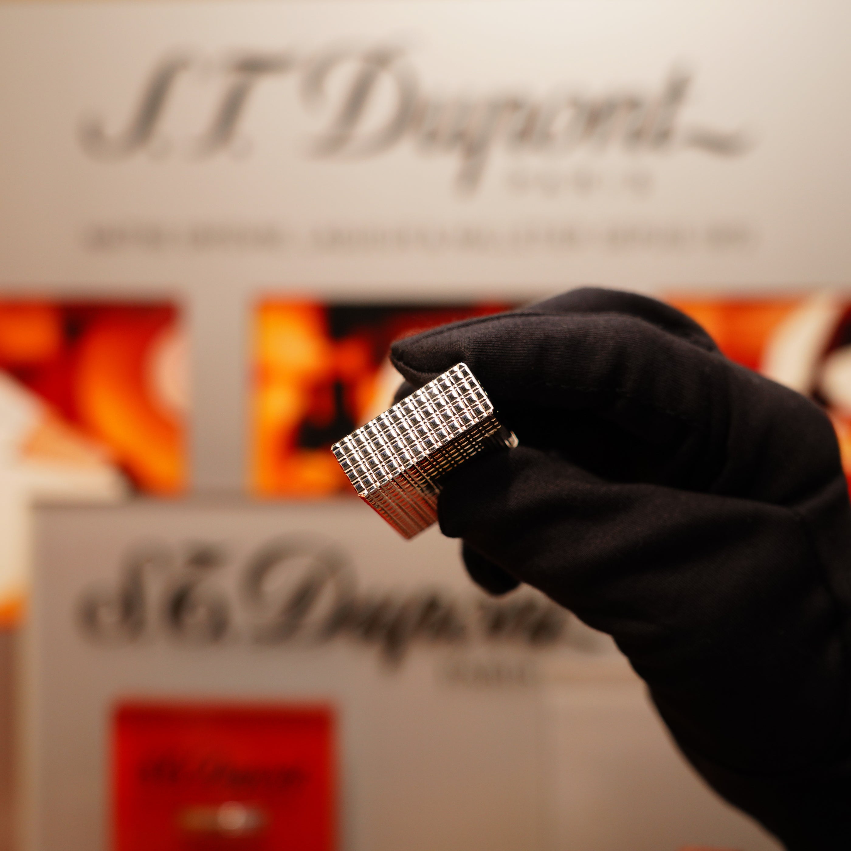 A gloved hand holds a rectangular silver object with a grid pattern, identified as the "Vintage 1990 S.T. Dupont Heavy Silver Finish Iconic Ligne 1 Rare Window Pattern Lighter," in front of a blurred S.T. Dupont logo backdrop.