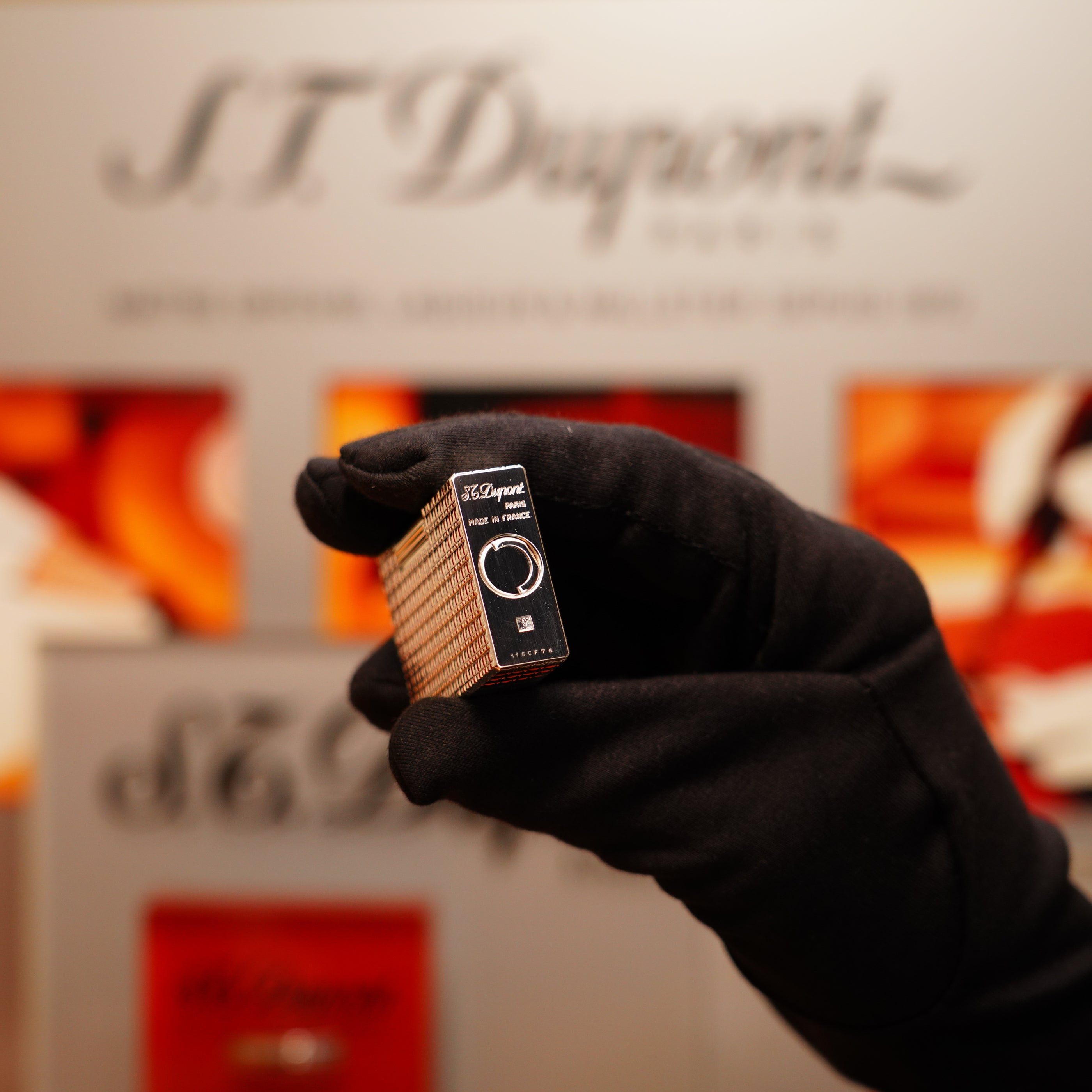 A gloved hand holds a rare Vintage 1990 St Dupont Heavy Silver Finish Iconic Ligne 1 lighter with a window pattern in front of a blurred background displaying the brand, S.T. Dupont.