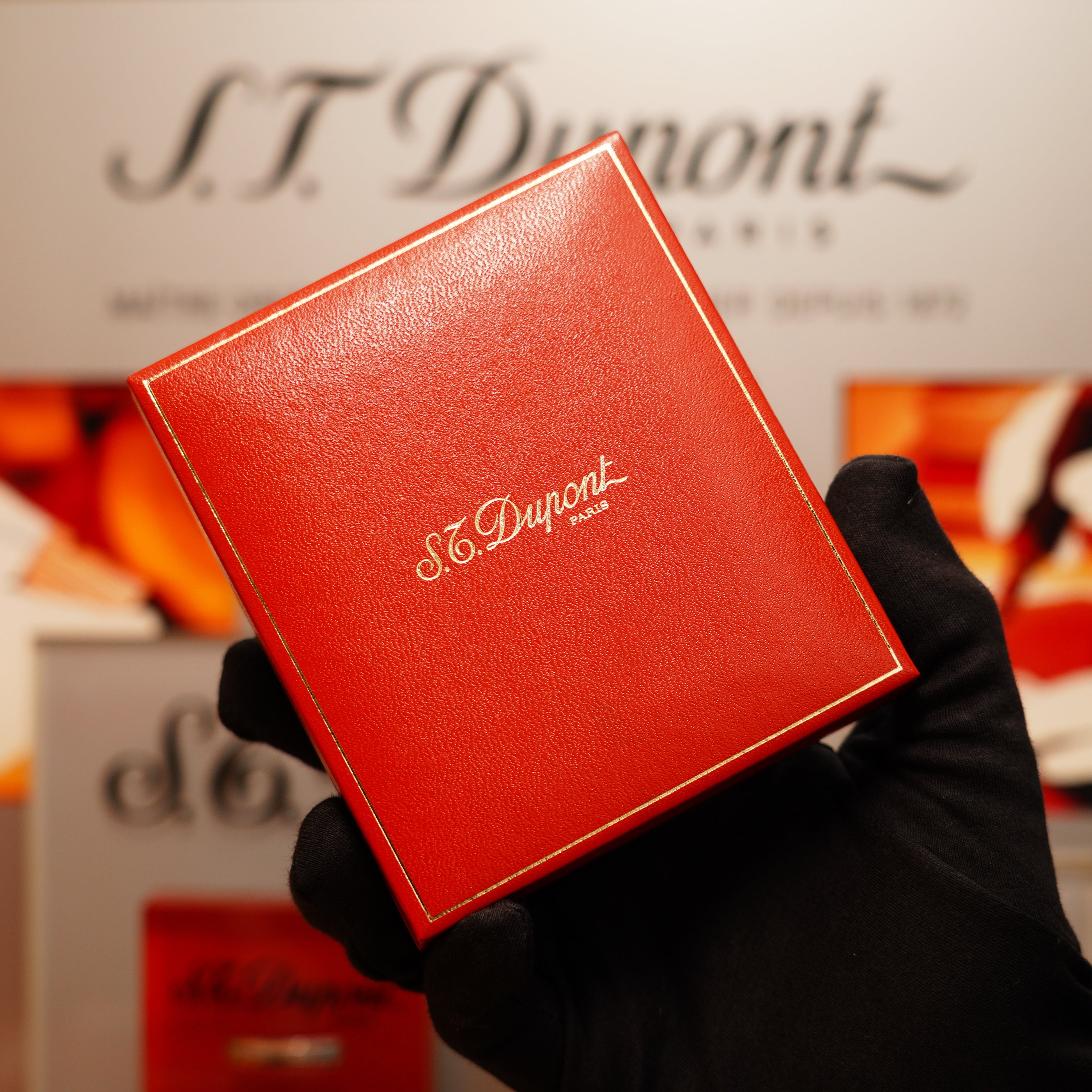 A person in black gloves holds a red S.T. Dupont Paris box against a blurred backdrop featuring the Vintage 1990 St Dupont Heavy Silver Finish Iconic Ligne 1 Rare Window Pattern Lighter.