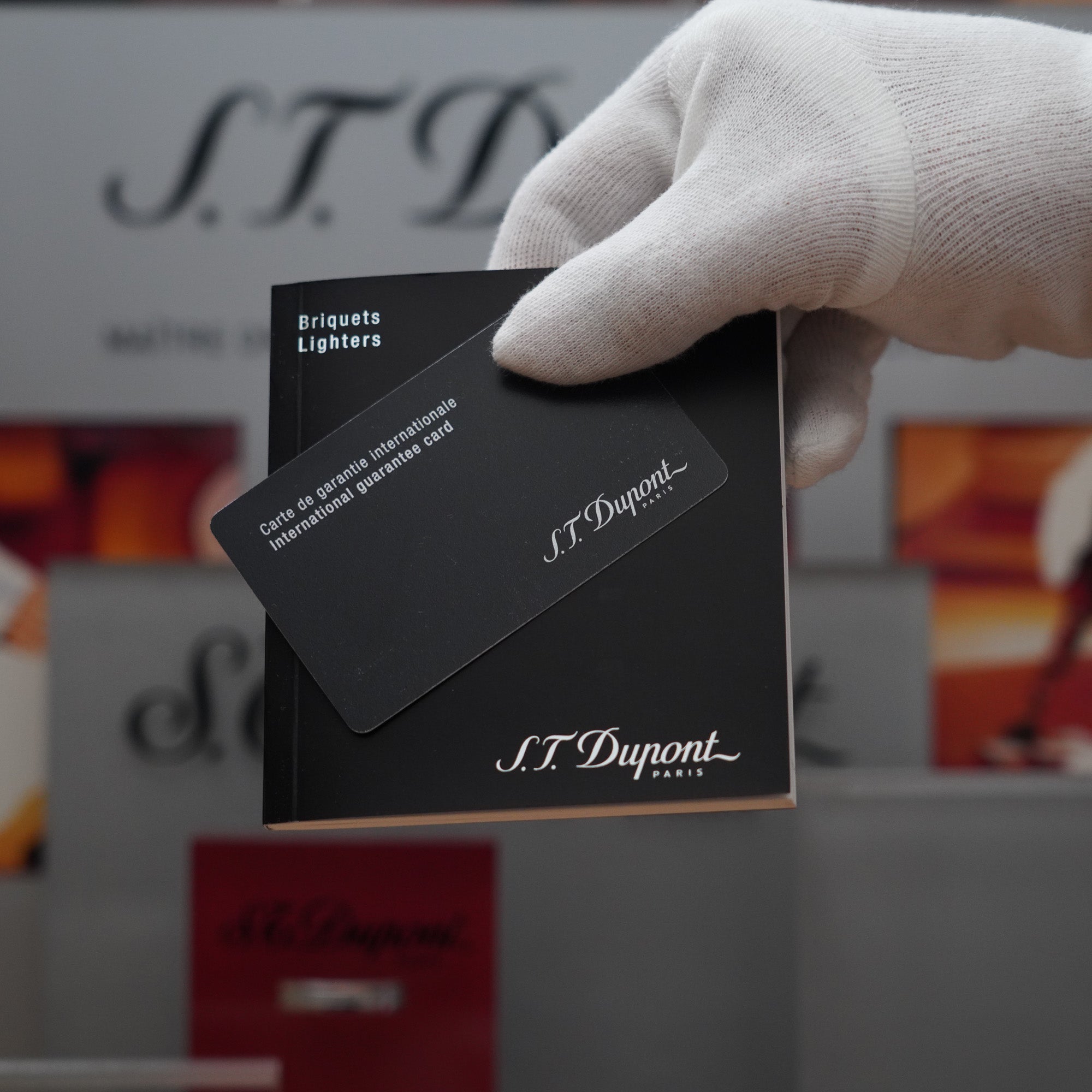 A hand holding a black card in front of a display featuring Vintage 2000 S.T. Dupont Palladium Décor High Tech 2000s Lighter.