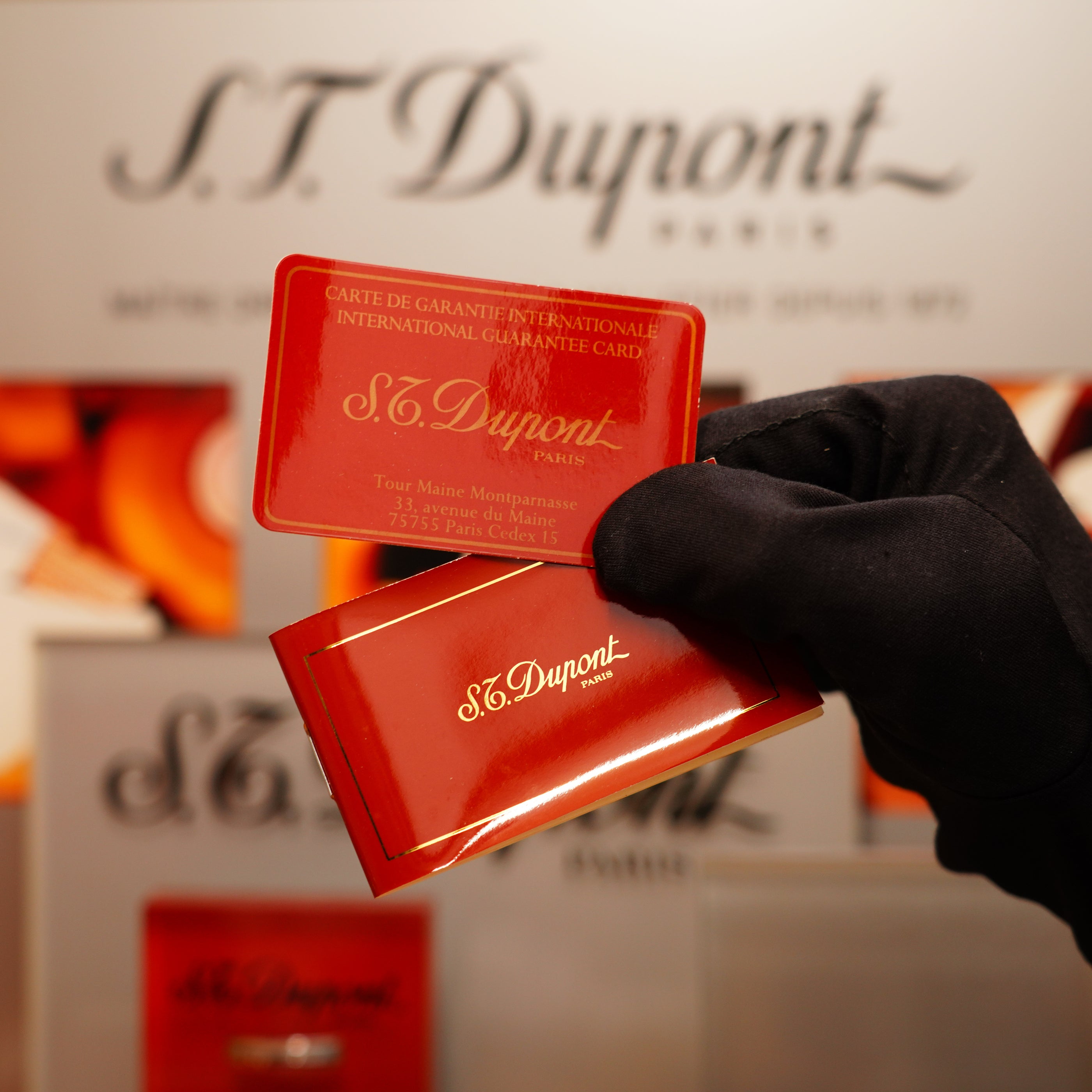 A gloved hand holds the Vintage 1990 S.T. Dupont 24k Gold Iconic Ligne 1 Diamond Head Pattern Lighter, two in number, in front of a display.