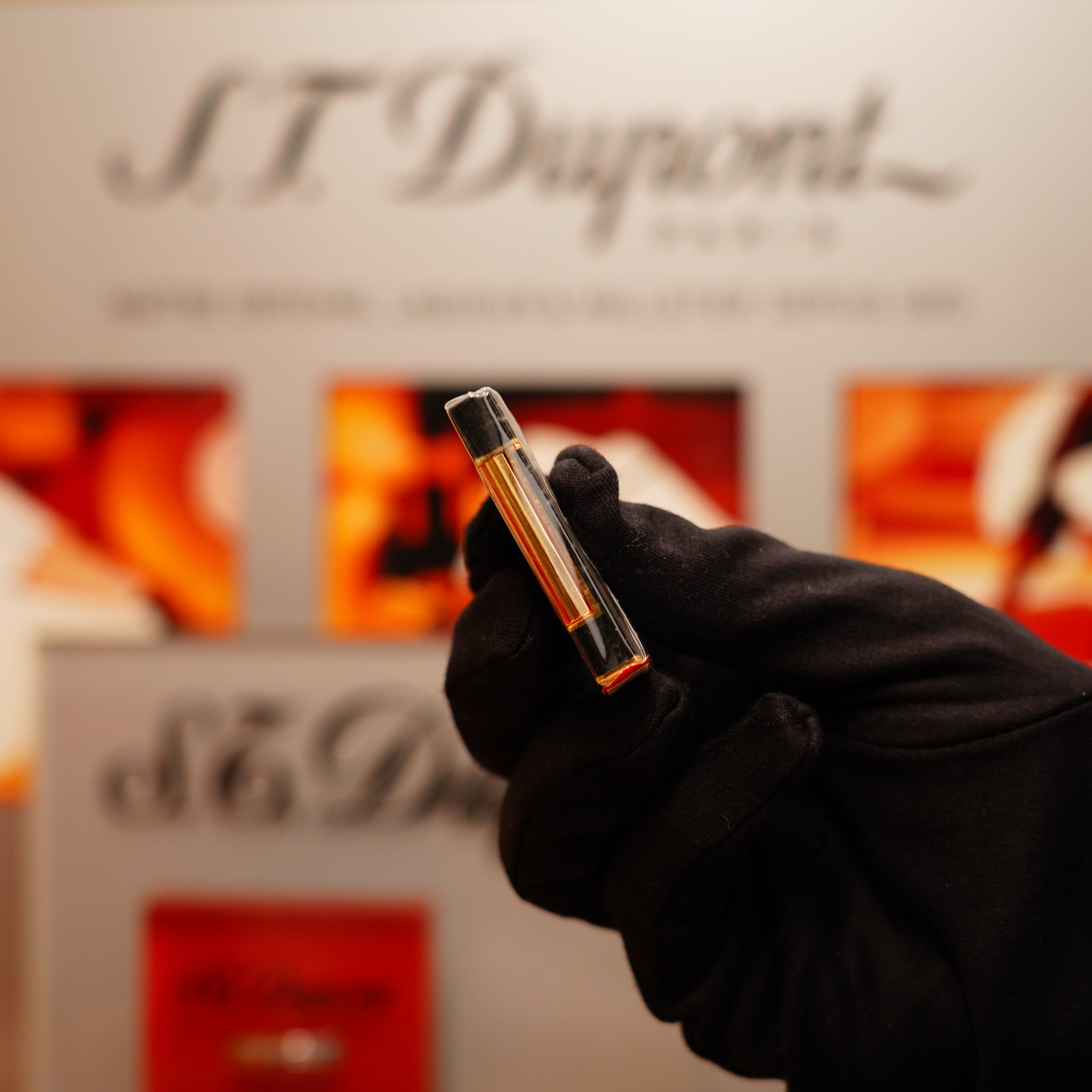 A gloved hand holds a slim, gold rectangular object against a blurred S.T. Dupont backdrop, featuring the Vintage 1990 St Dupont Overall Black Lacquer Early 24k Gold Ligne D Sealed Lighter.