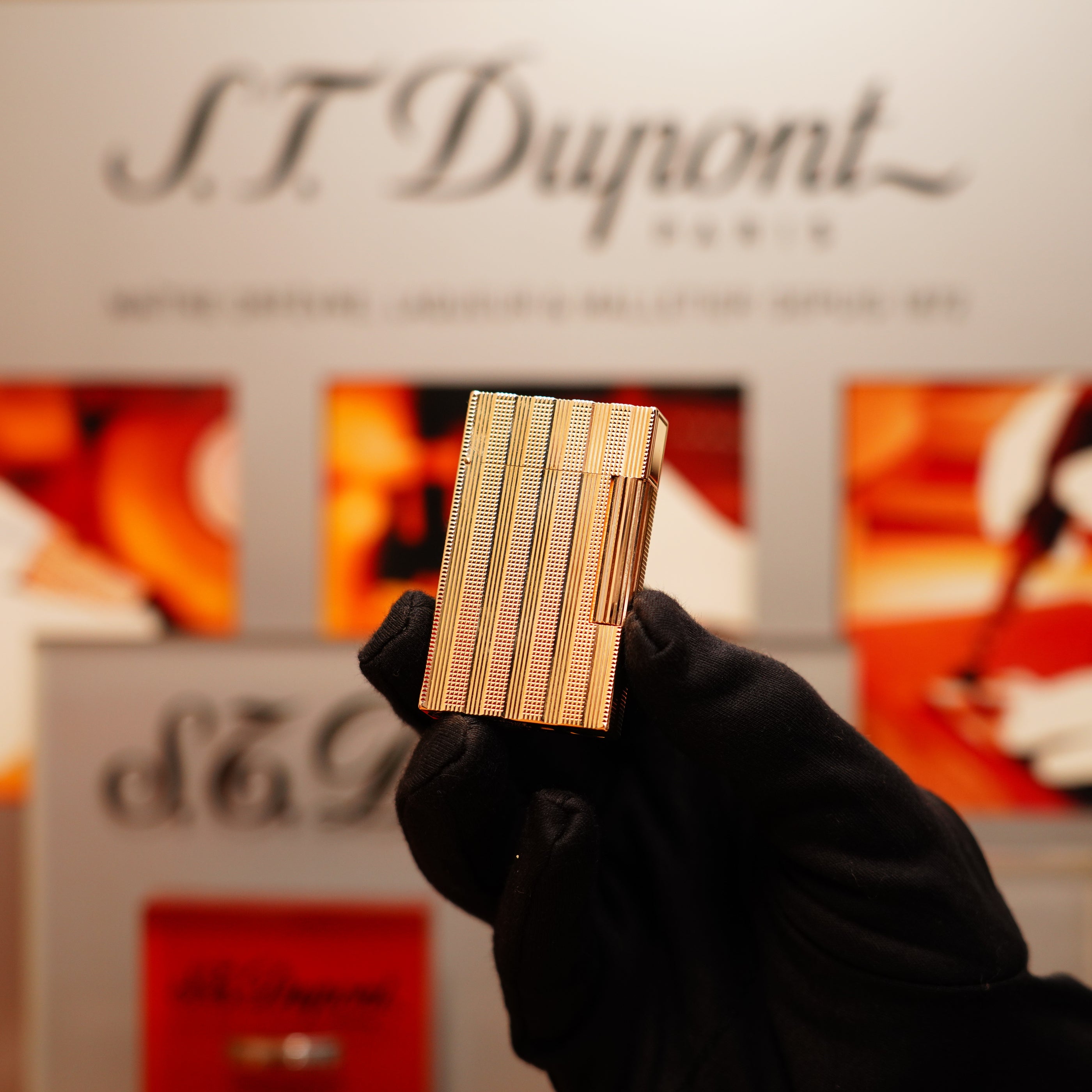 A gloved hand holds a Vintage 1978 S.T. Dupont 24k Gold Lignes Verticales Pointes Diamants Large Ligne 2 lighter against a blurred background with S.T. Dupont branding.