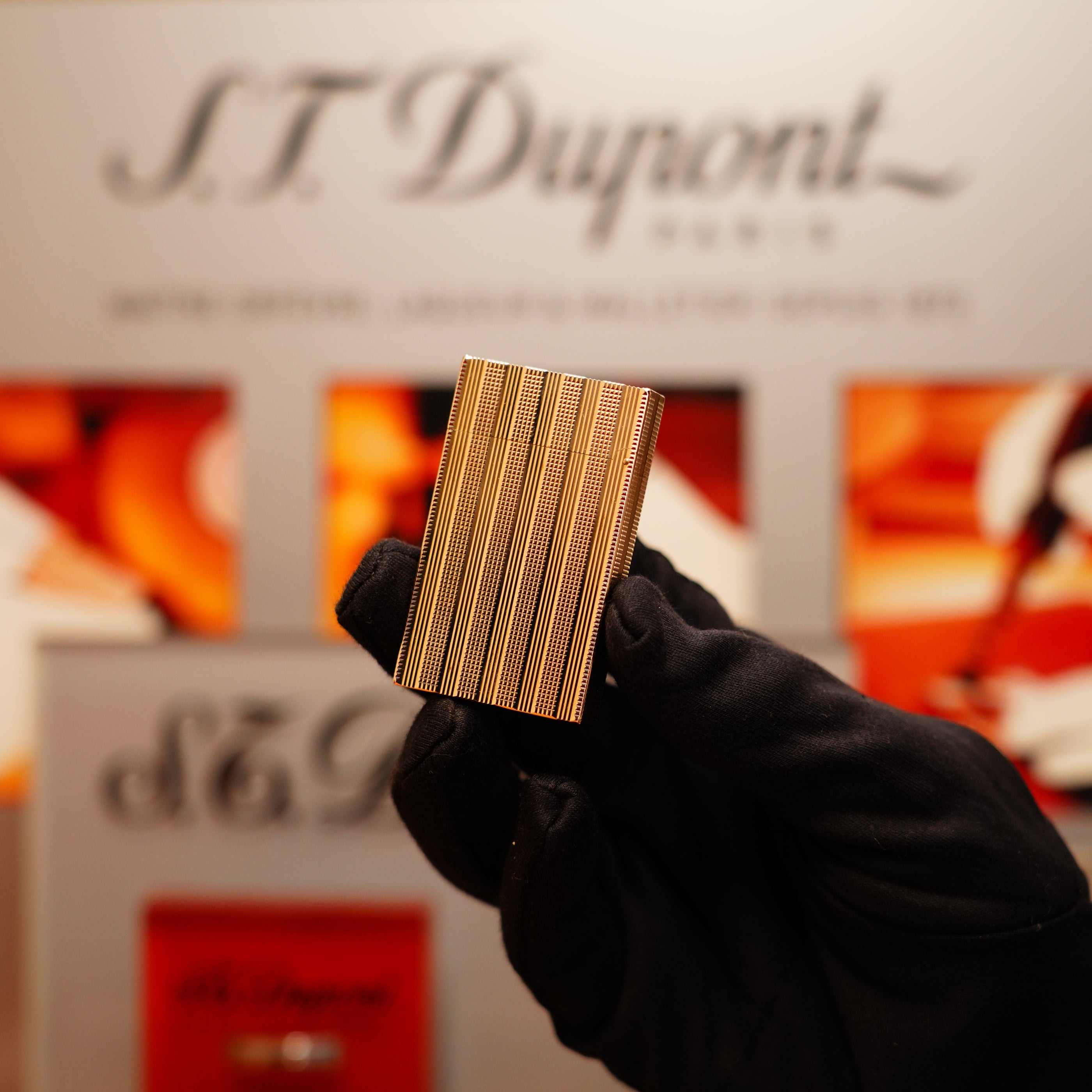 A gloved hand holds a Vintage 1978 S.T. Dupont 24k Gold Lignes Verticales Pointes Diamants Large Ligne 2 Lighter before a blurred ST Dupont display.