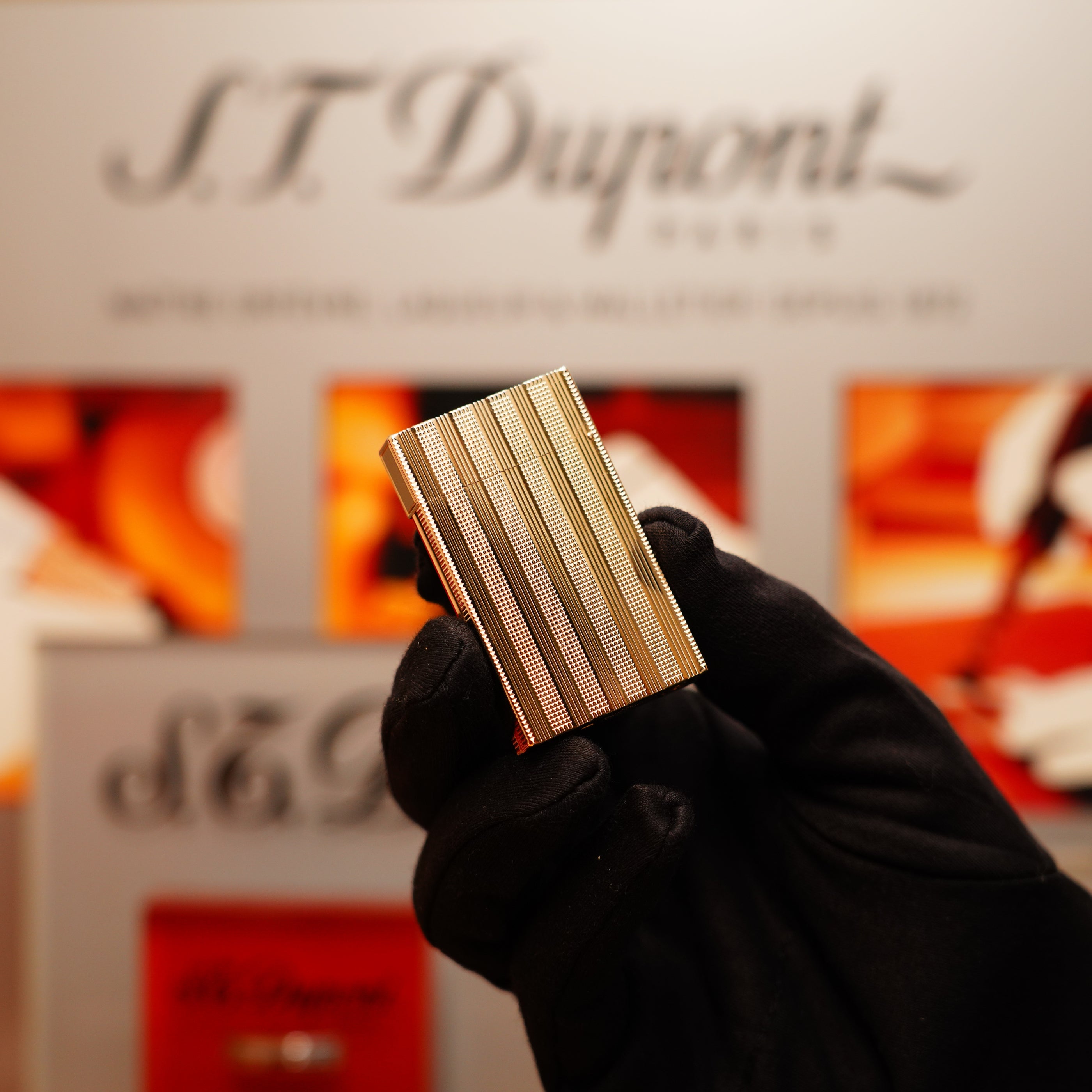 A person wearing black gloves holds a Vintage 1978 S.T. Dupont 24k gold Ligne 2 lighter in front of a blurred brand display.