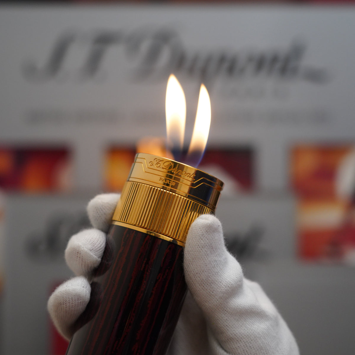 Vintage 1980 S.T. Dupont hand holding a lit candle on a Vintage 1980 S.T. Dupont 18k Masterpiece Unique Cylinder Gold Plated Macassar Lacquer Dual Flame Table Lighter.