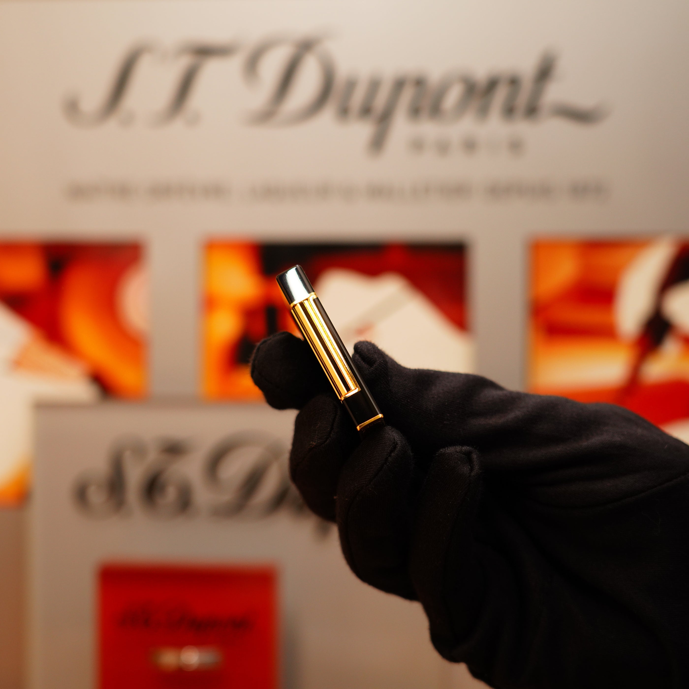 A gloved hand holds a Vintage 1990 St Dupont Overall Black Lacquer Early 24k Gold Ligne D Lighter against a blurred background with the S.T. Dupont logo.