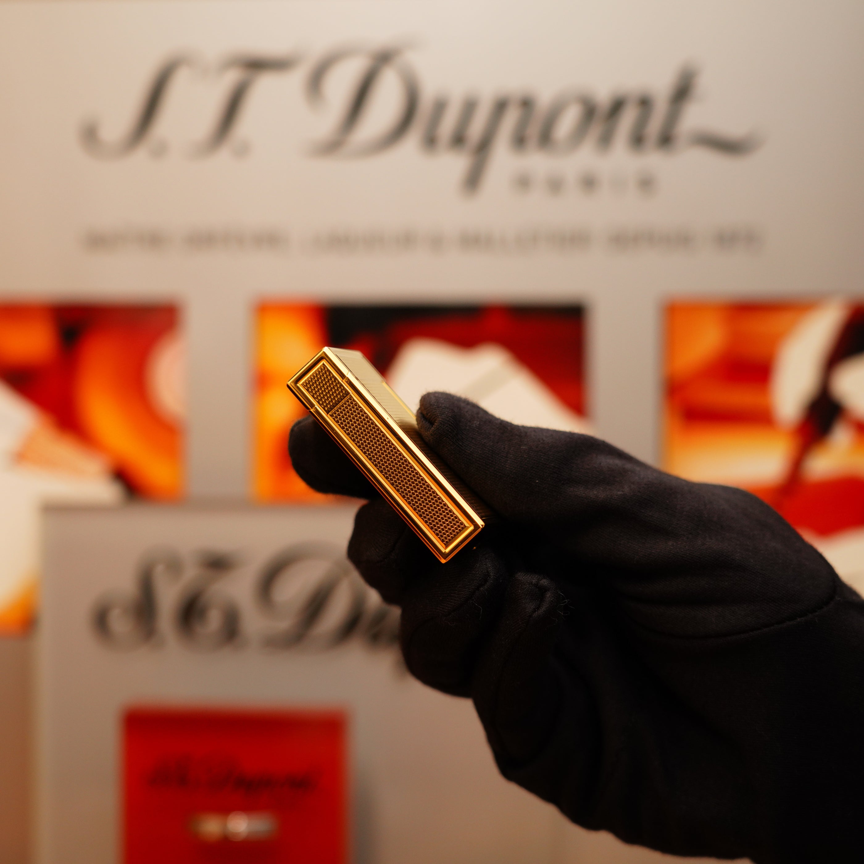 A gloved hand holds a Vintage 1990 S.T. Dupont 24k Large Grain d'Org Iconic Ligne 1 Heavy Finish Lighter, shown against a blurred backdrop with the brand's logo.