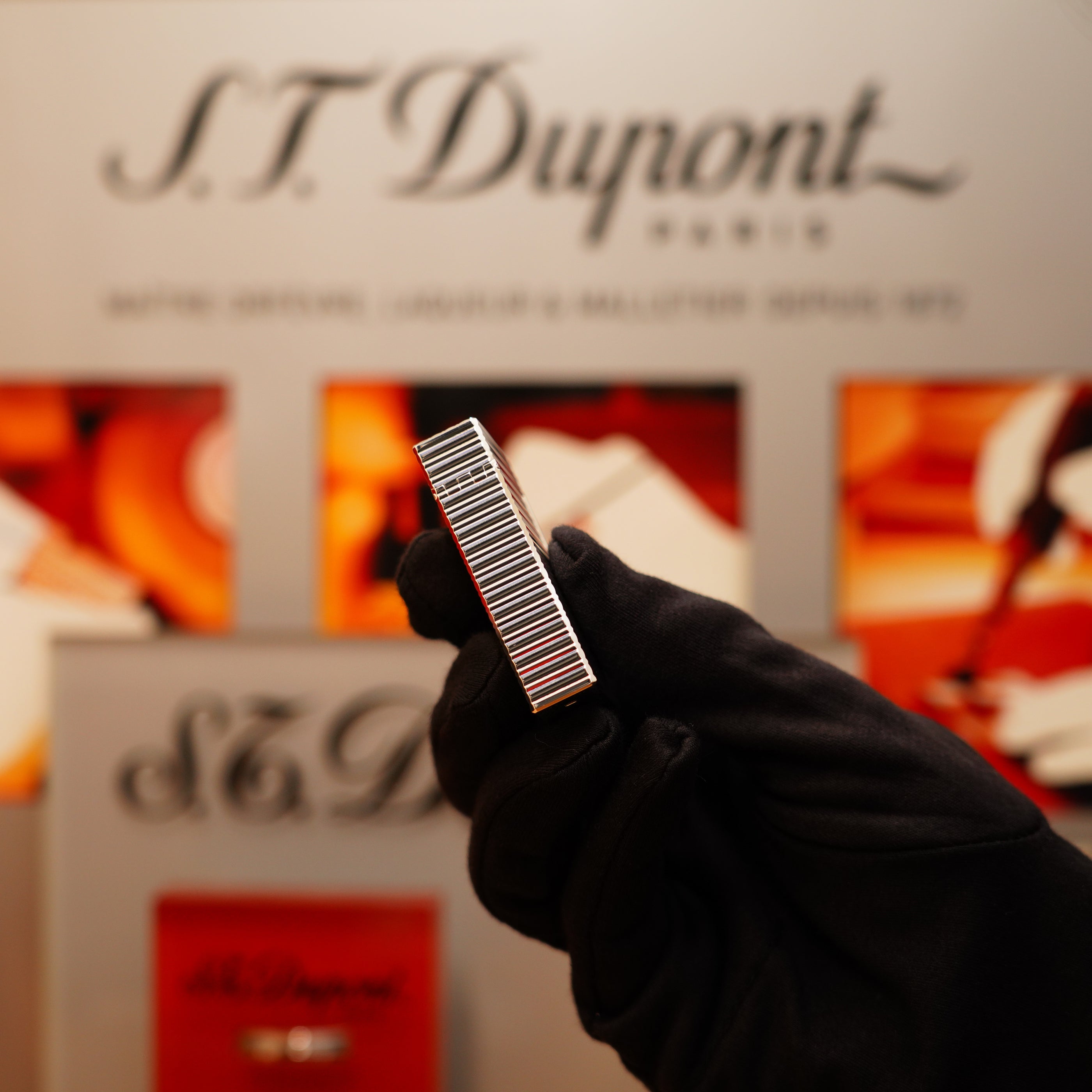 A person in a black glove holds a Vintage 1990 S.T. Dupont Ligne 1 Horizontal Pattern Lighter with a heavy silver finish before an S.T. Dupont Paris display.