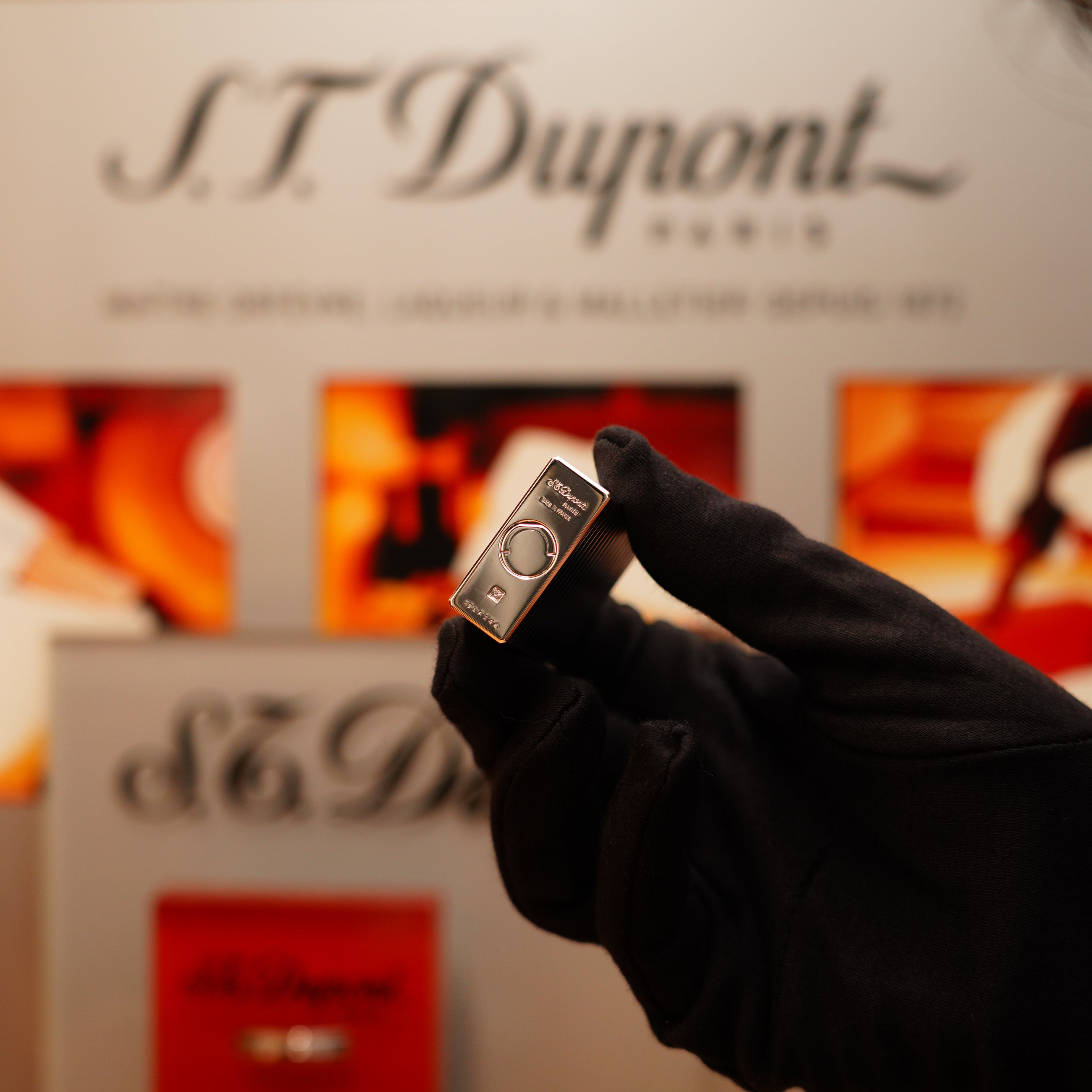 A gloved hand holds a Vintage 1990 S.T. Dupont Ligne 1 Silver Finish Horizontal Pattern Lighter in front of a blurred brand display background.