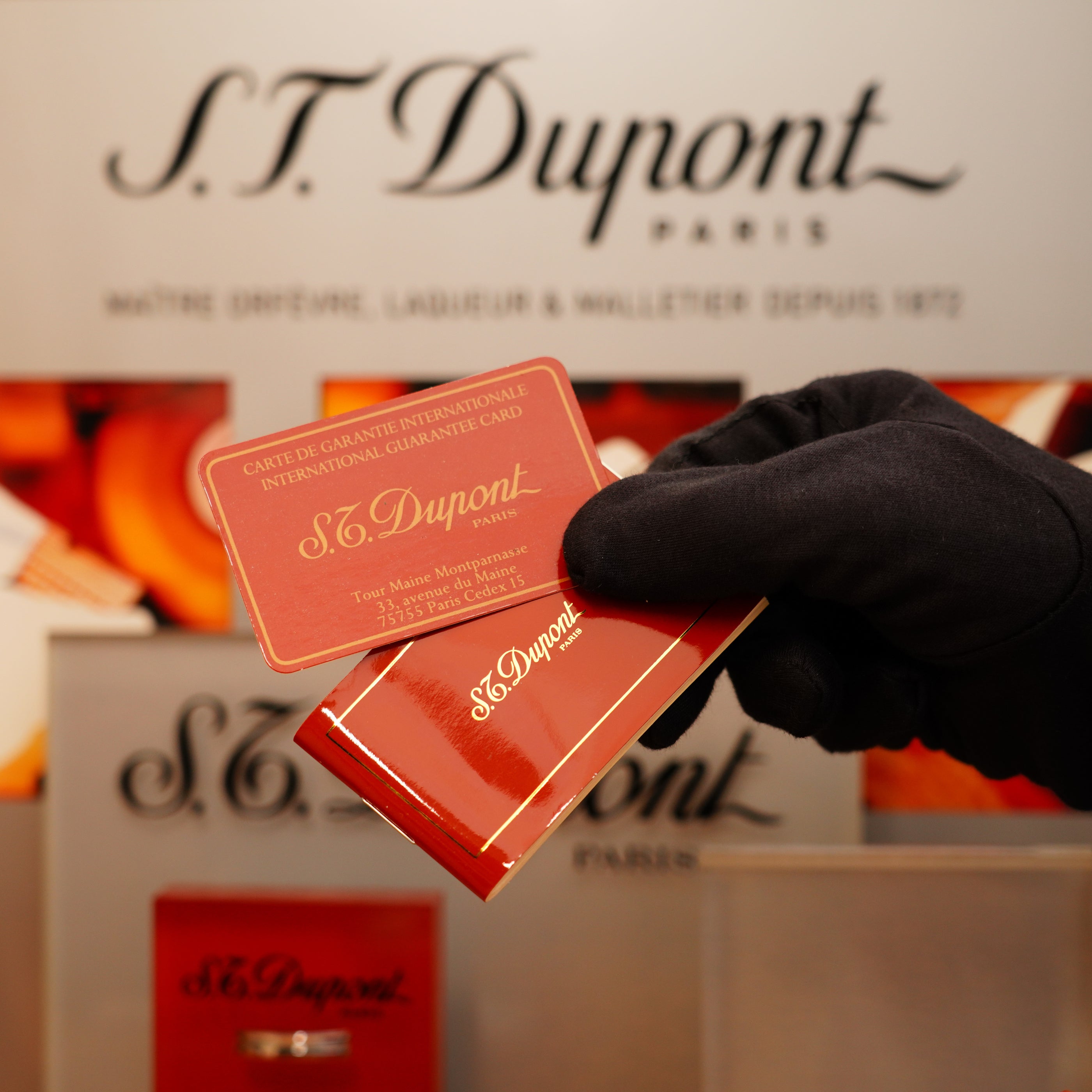 A gloved hand holds a Vintage 1990 S.T. Dupont Large Heavy Silver Finish Ligne 1 Horizontal Pattern Lighter and an international guarantee card against a branded background.