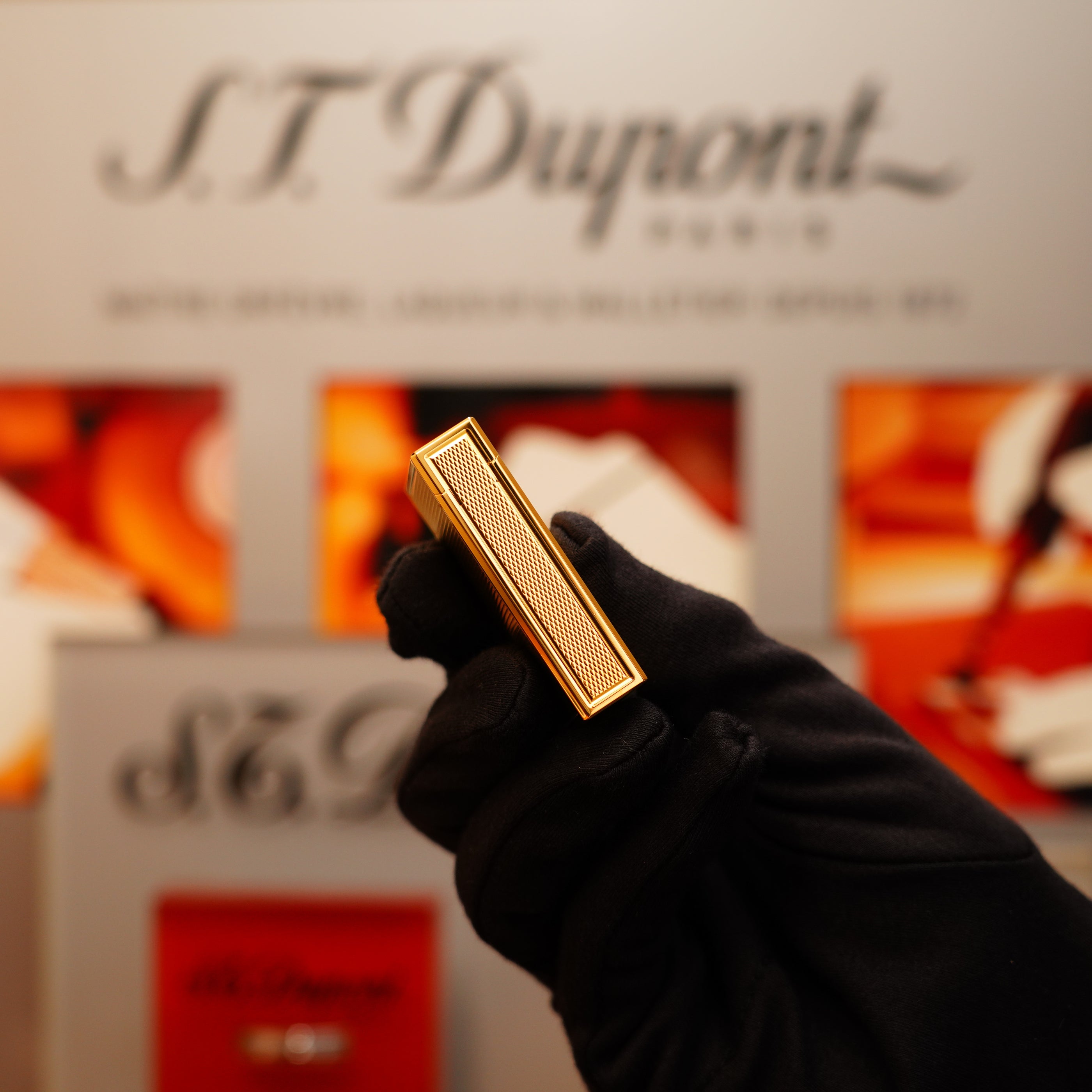 A gloved hand holds a Vintage 1994 S.T. Dupont 24k Large Grain d'Org Iconic Ligne 1 lighter with a textured surface in front of an S.T. Dupont display.