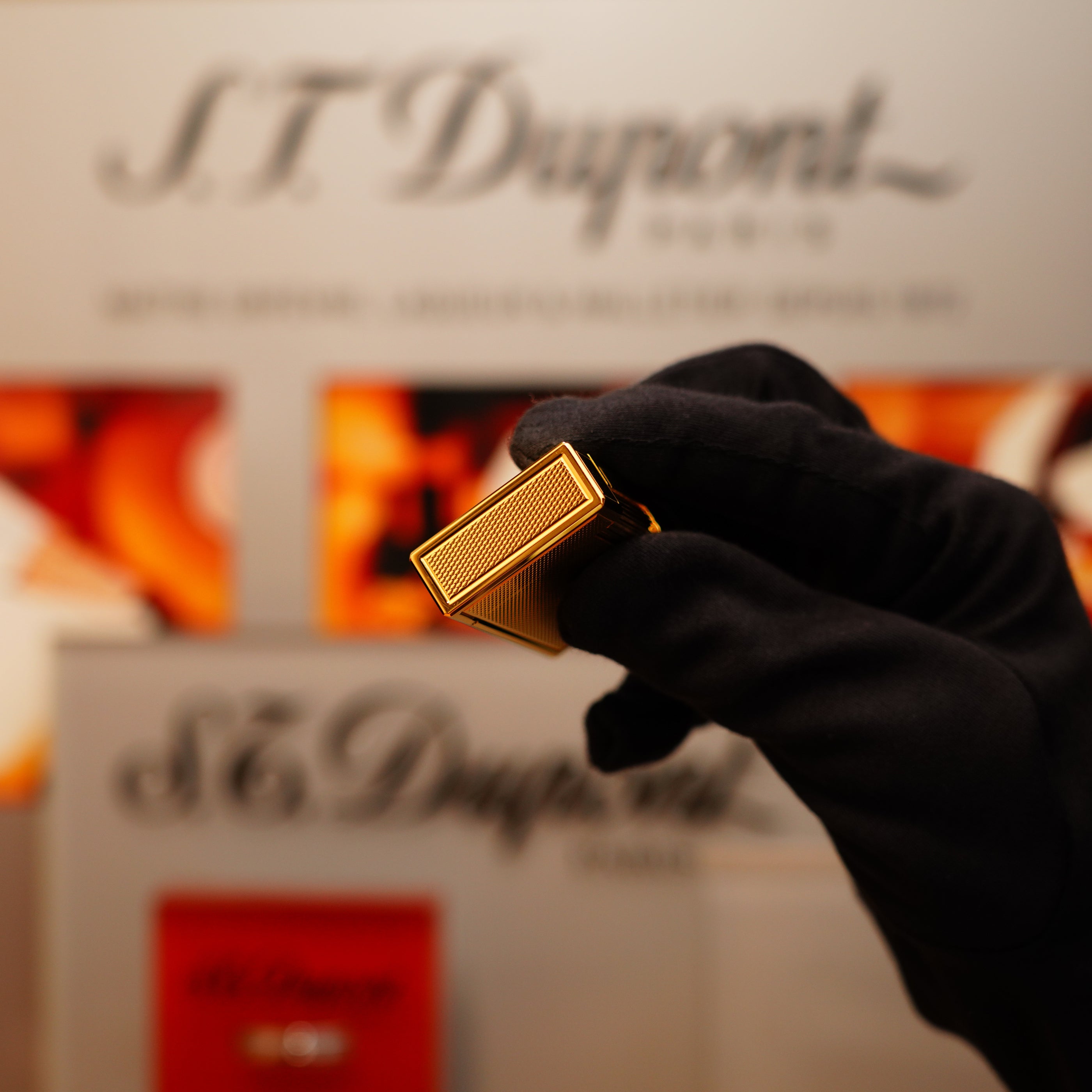 A person in black gloves holds a Vintage 1994 S.T. Dupont 24k Large Grain d'Org Ligne 1 lighter against a blurred branded backdrop.