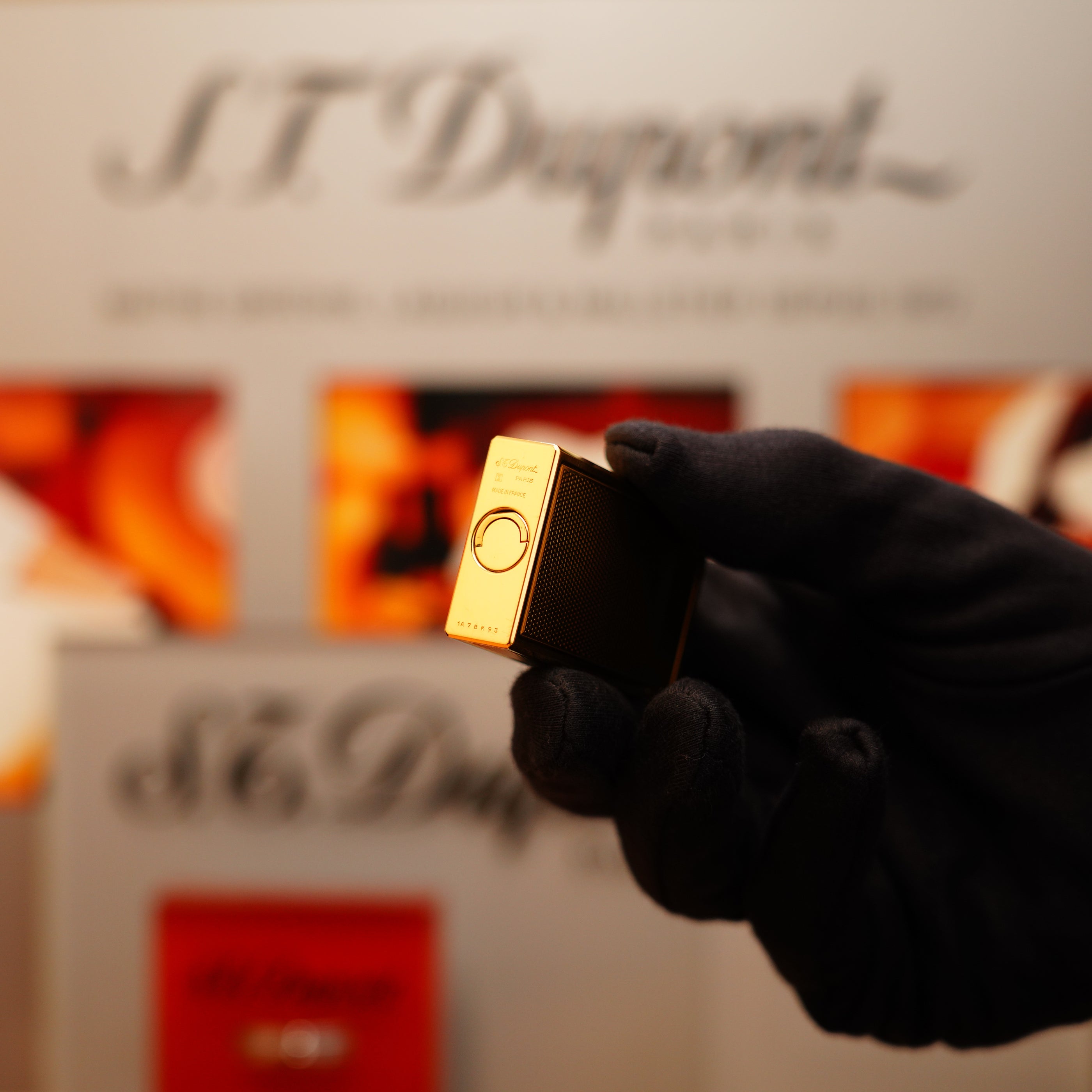 A gloved hand holds a luxury Vintage 1994 S.T. Dupont 24k Large Grain d'Org Iconic Ligne 1 lighter with a heavy finish against a blurred backdrop displaying the brand's name.