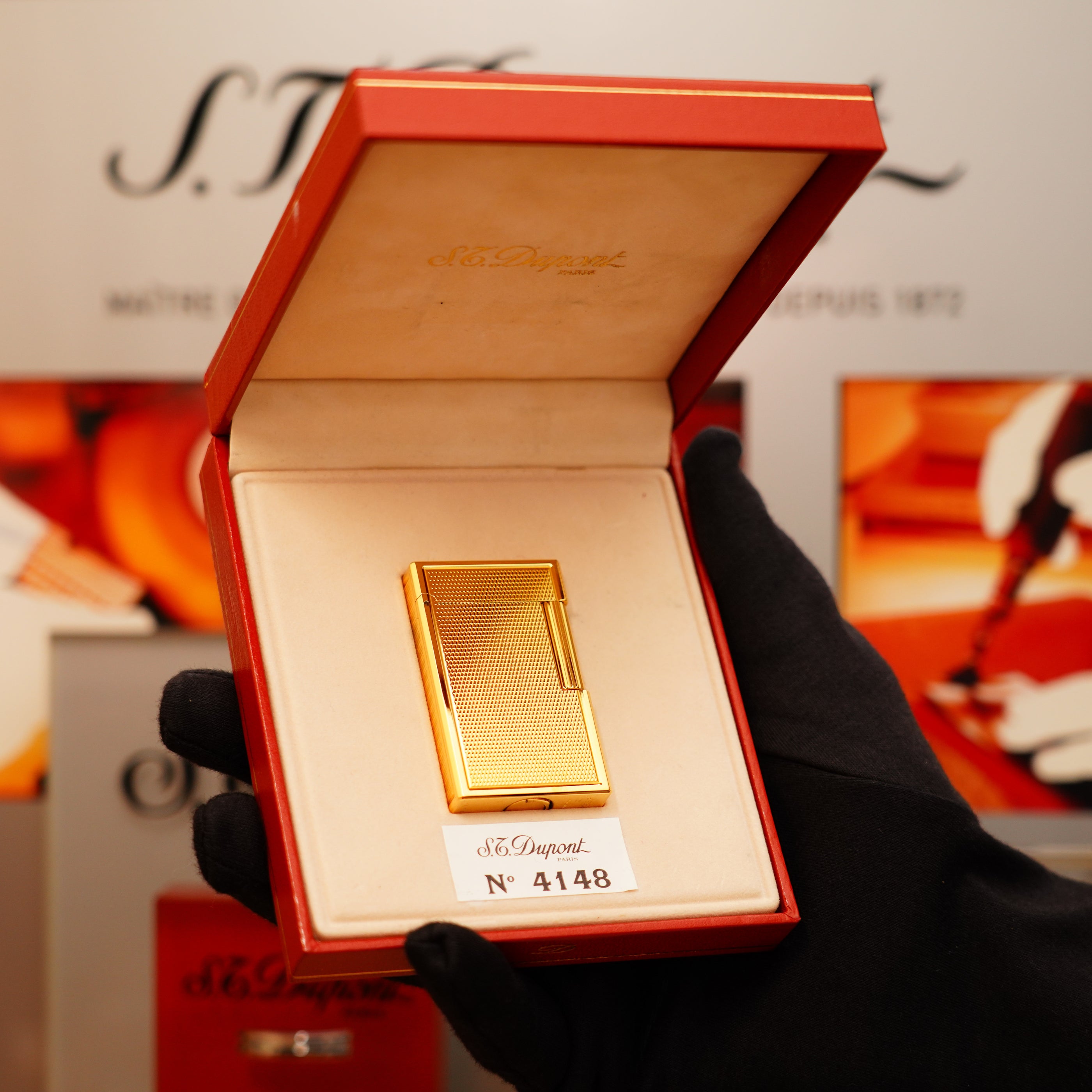 A golden S.T. Dupont lighter labeled "N° 4148" is displayed in a red box, opened by a gloved hand.